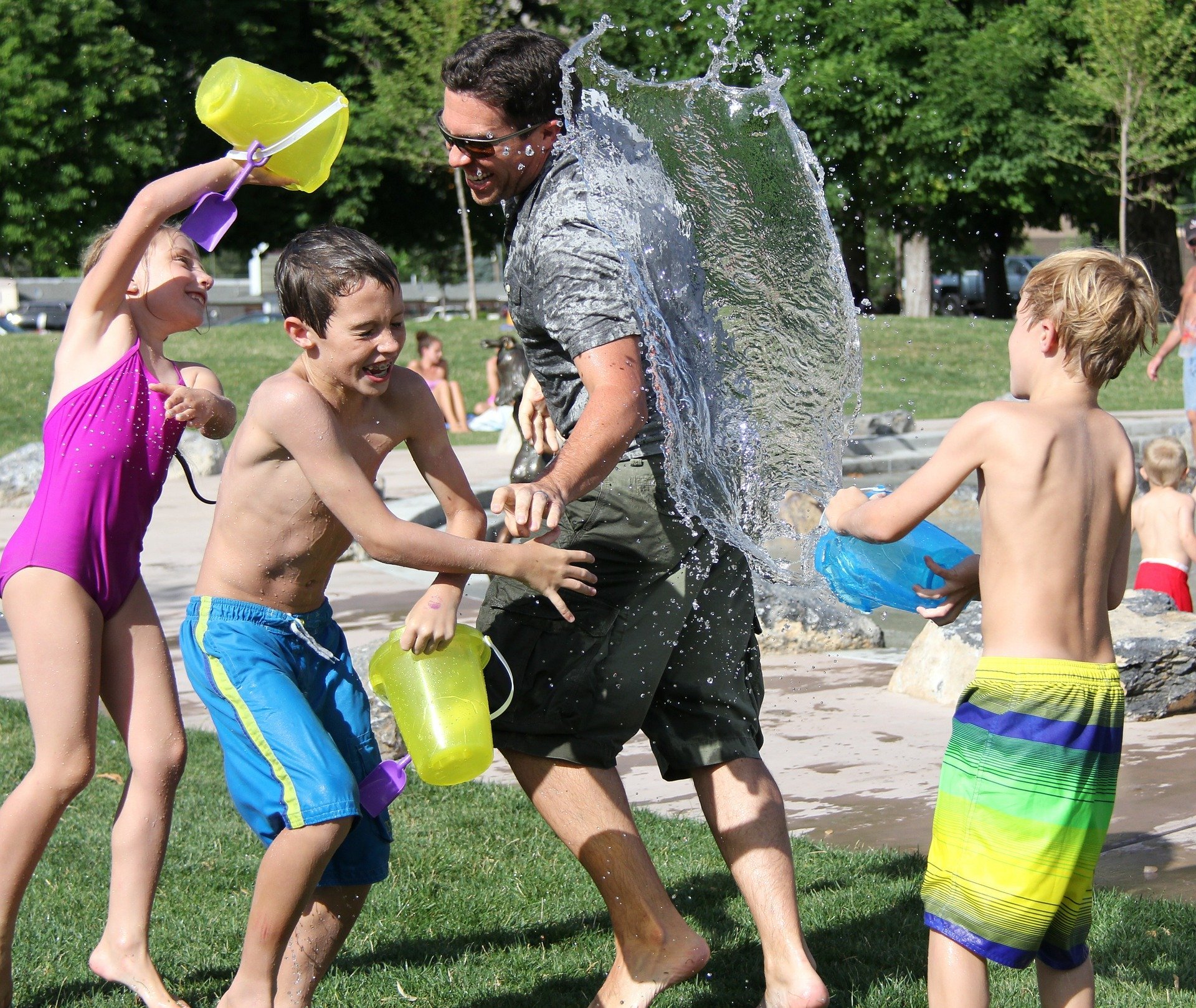 Homem brincando  com crianças ao ar livre, com baldes de água