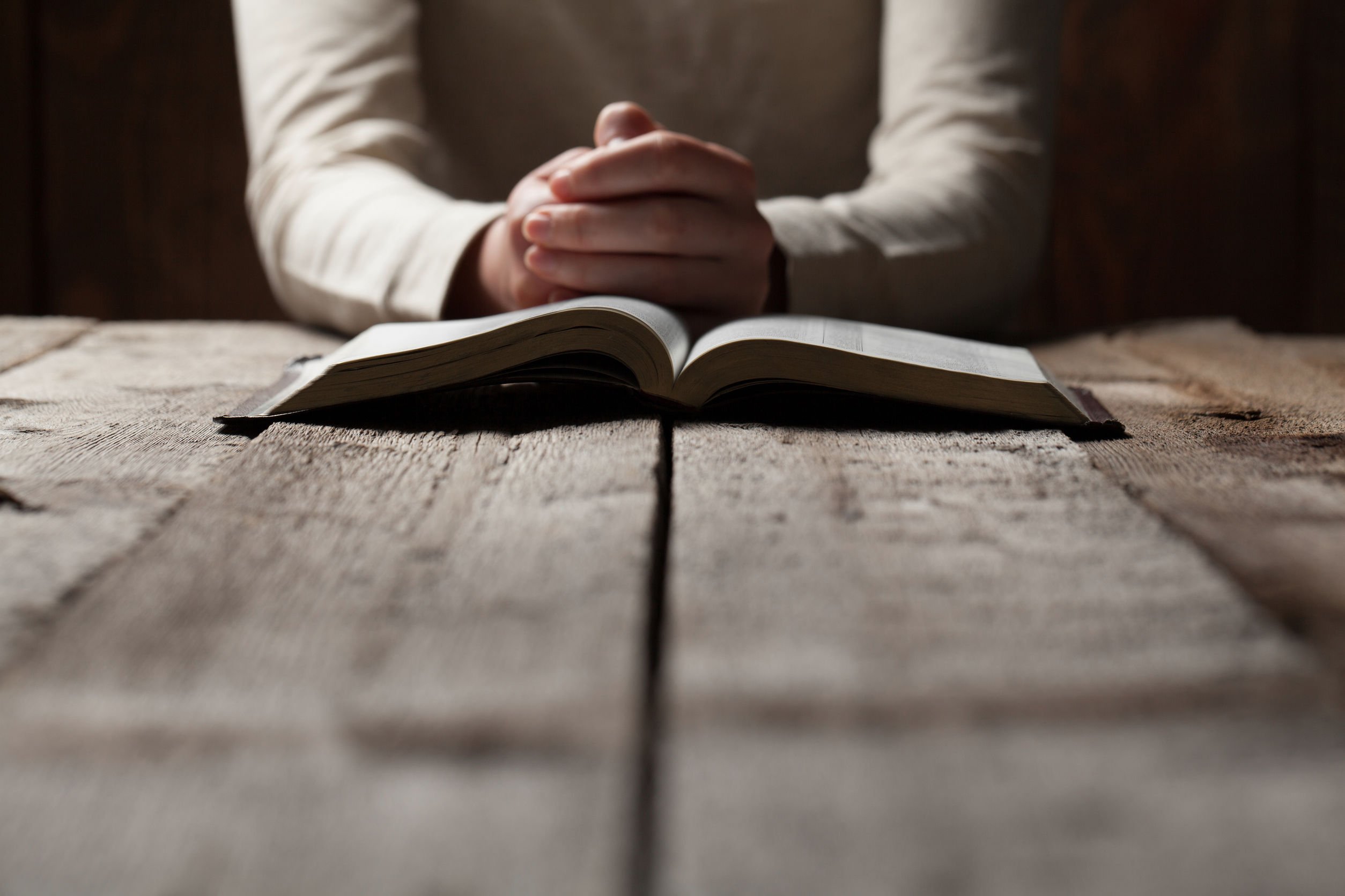 Homem orando com as mãos unidas sobre bíblia aberta em cima de mesa