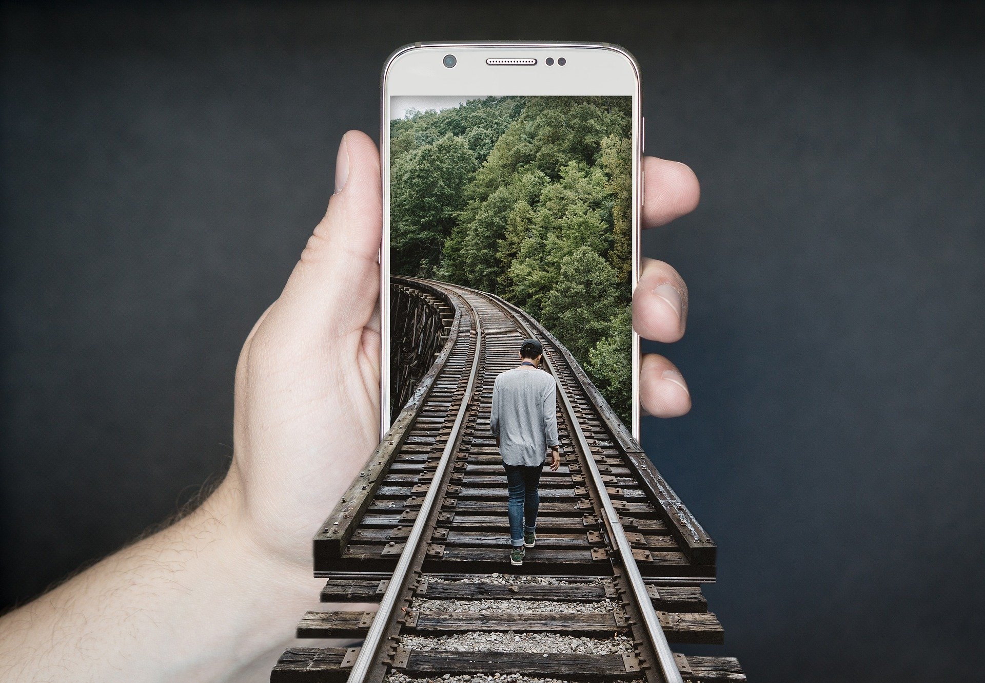 Pessoa segurando celular com desenho 3D de homem caminhando em trilho de trem saindo da tela do celular