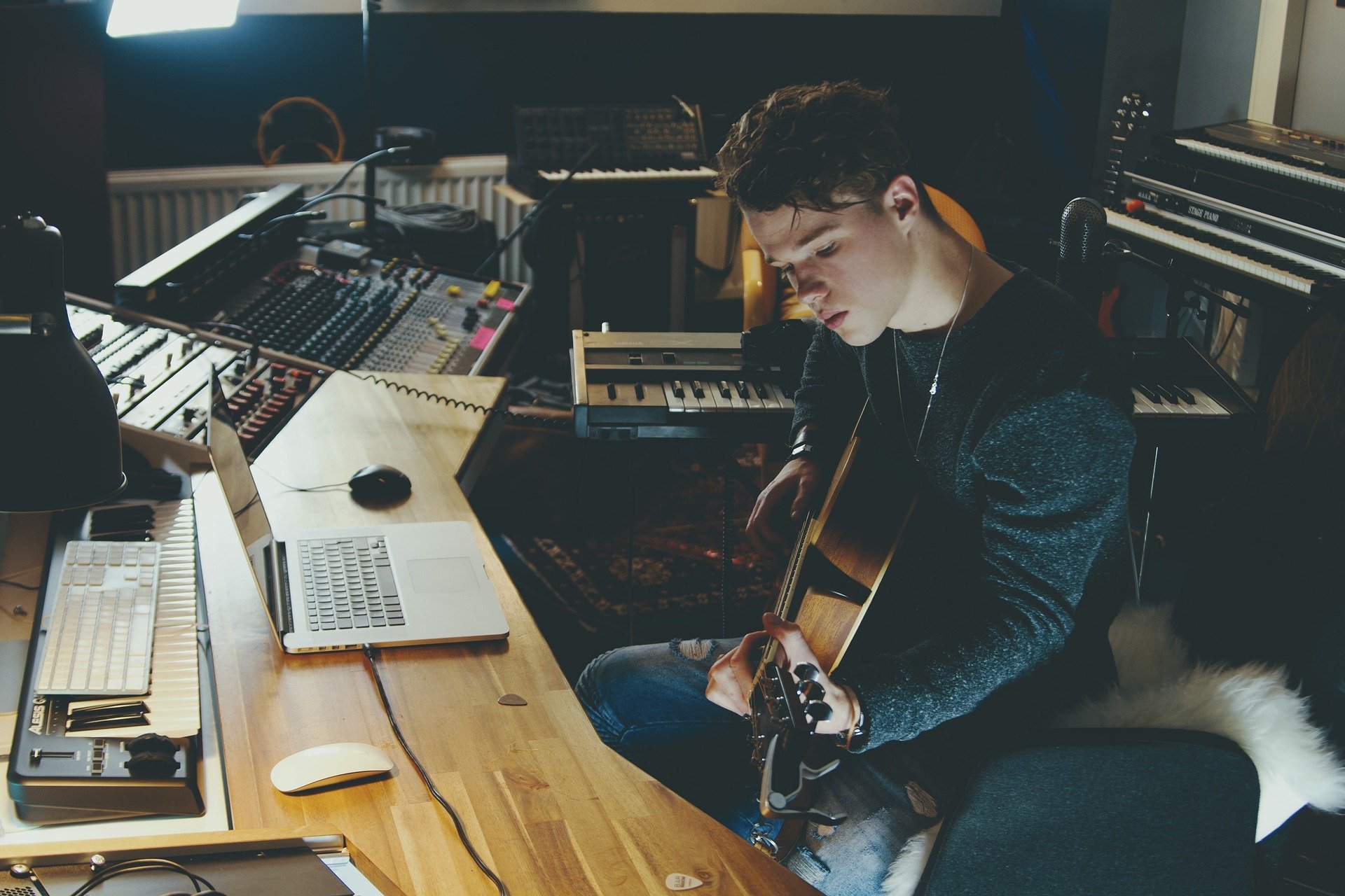 Homem jovem sentando em mesa de estúdio, tocando violão