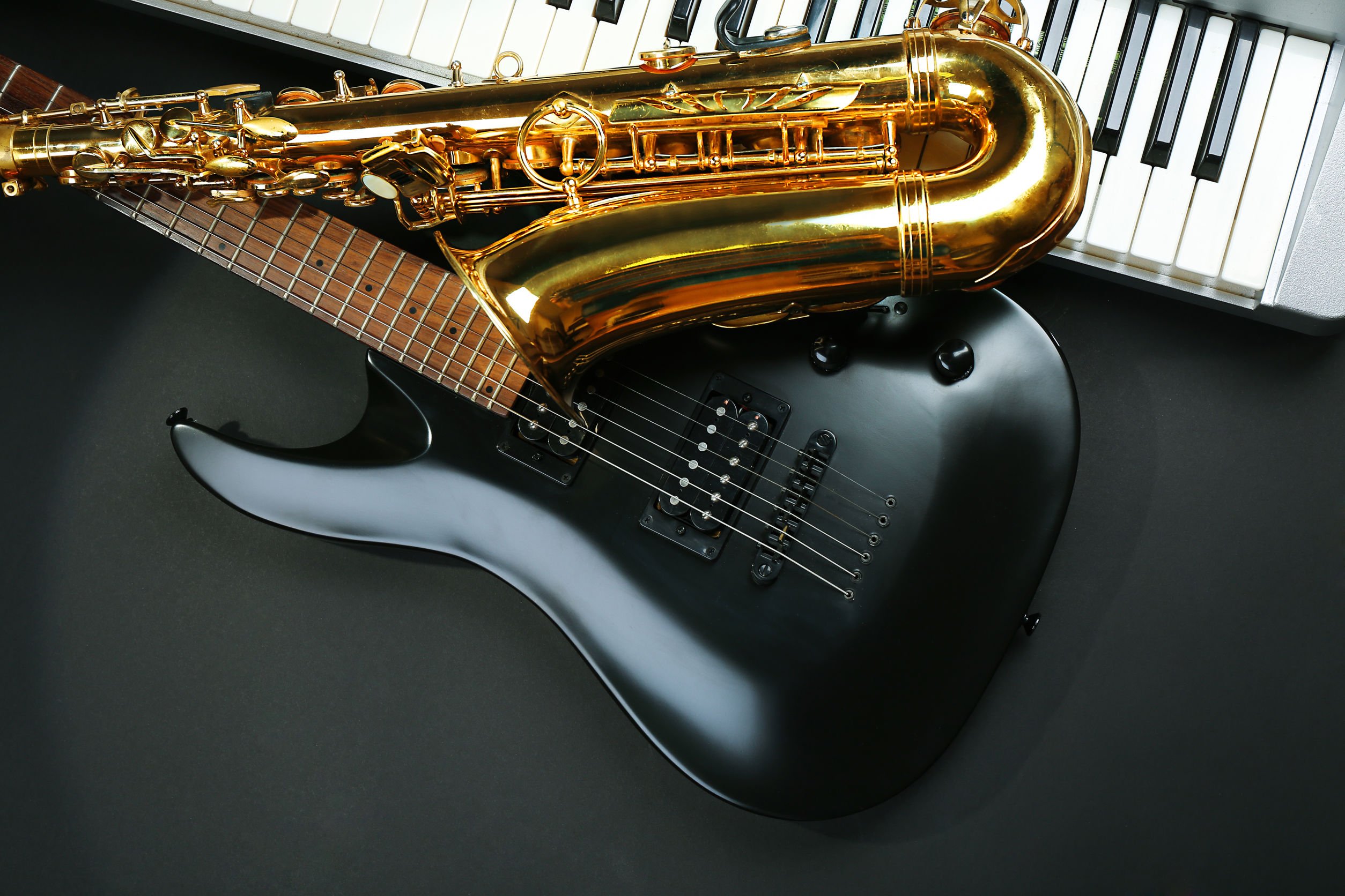 Saxofone, guitarra e teclado colocados lado a lado sobre fundo preto