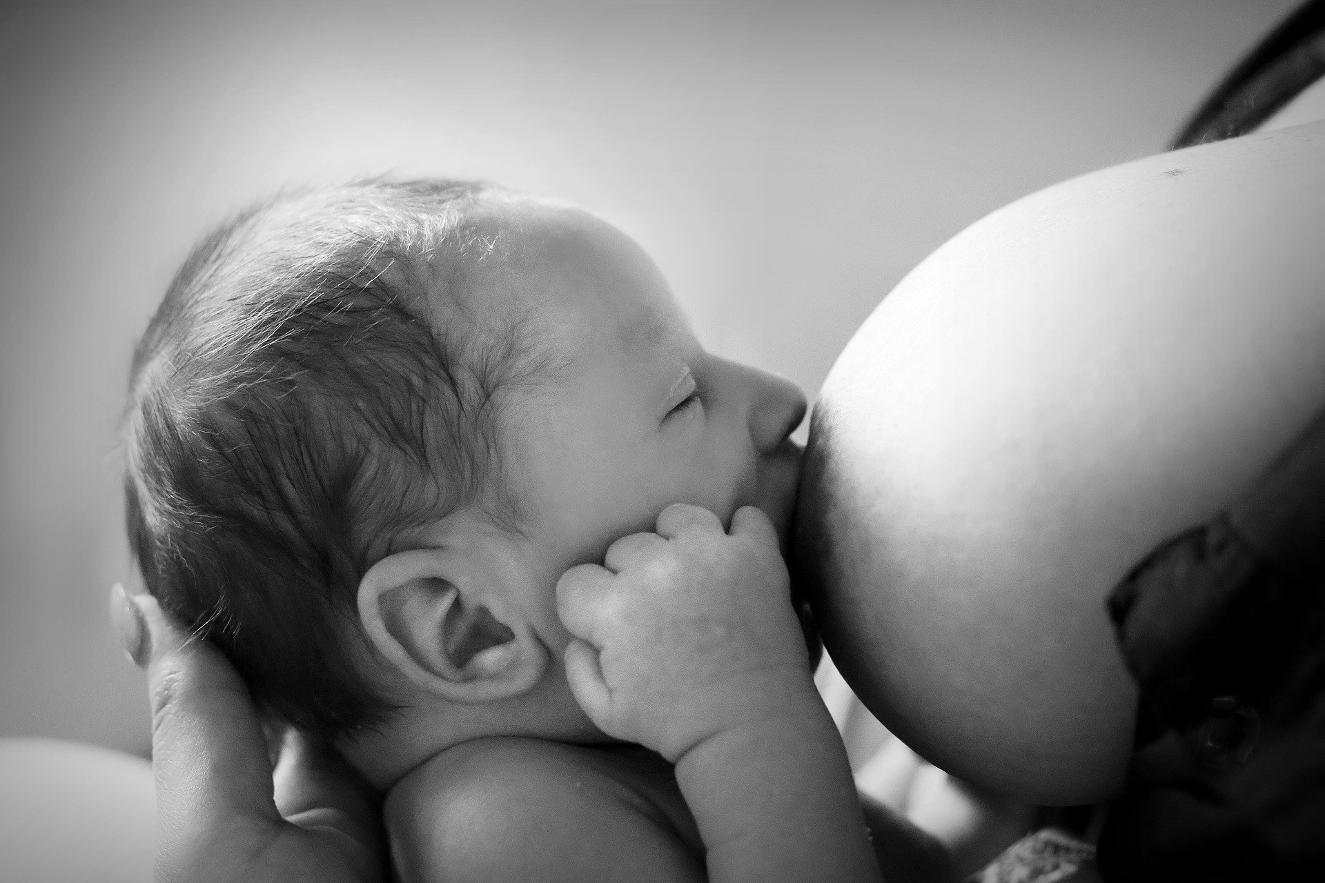 Foto preta e branca de bebê mamando em seio de mulher
