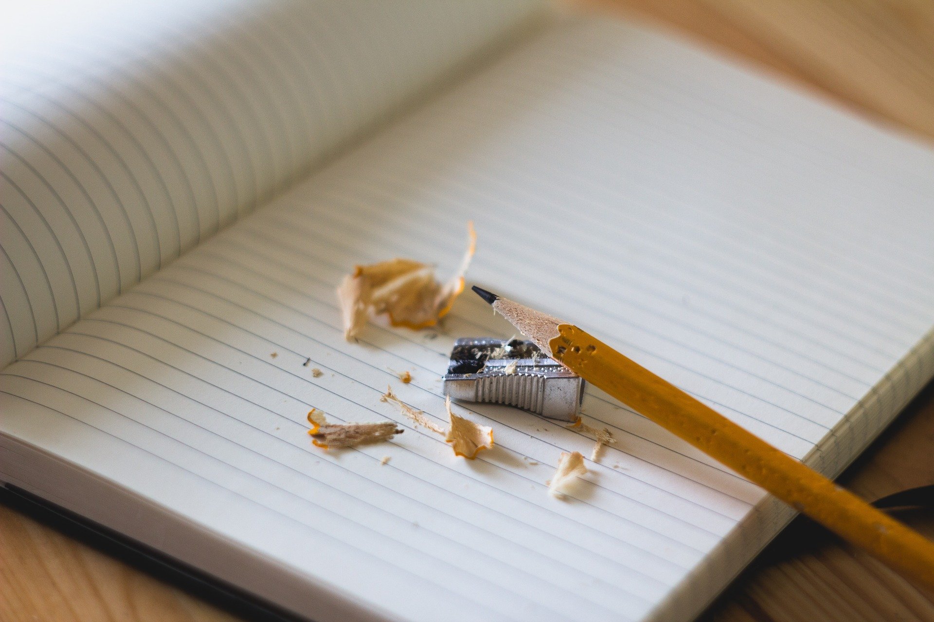 Lápis, apontador e cascas de lápis em cima de caderno aberto