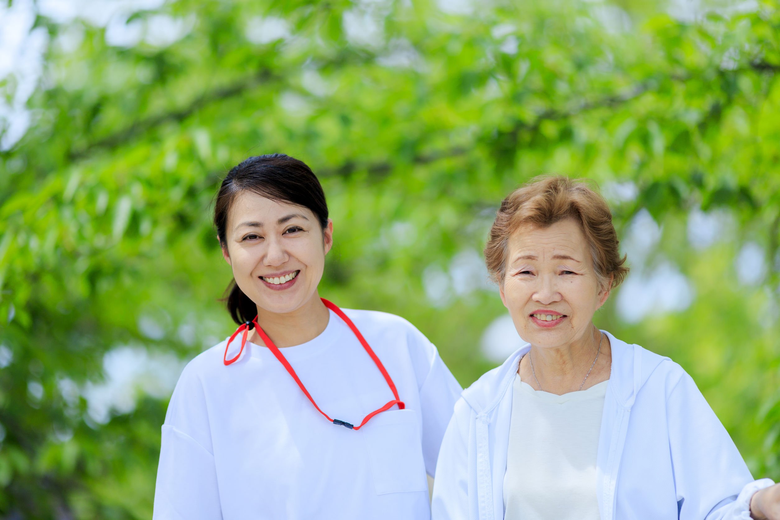 Mulher e senhora idosa, ambas são asiáticas e estão ao ar livre, sorrindo