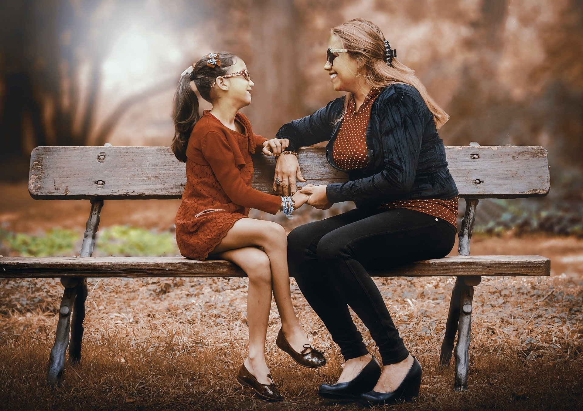 Mulher e filha sentada em banco de parque durante de outono