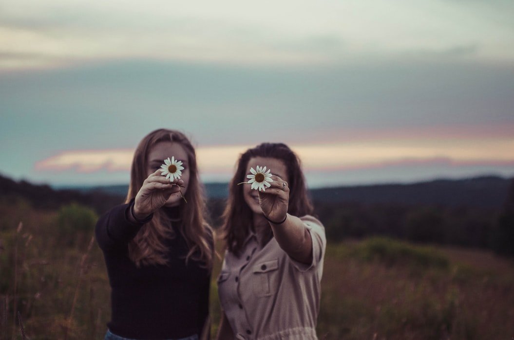 Mulheres amigas segurando flor em frente ao rosto