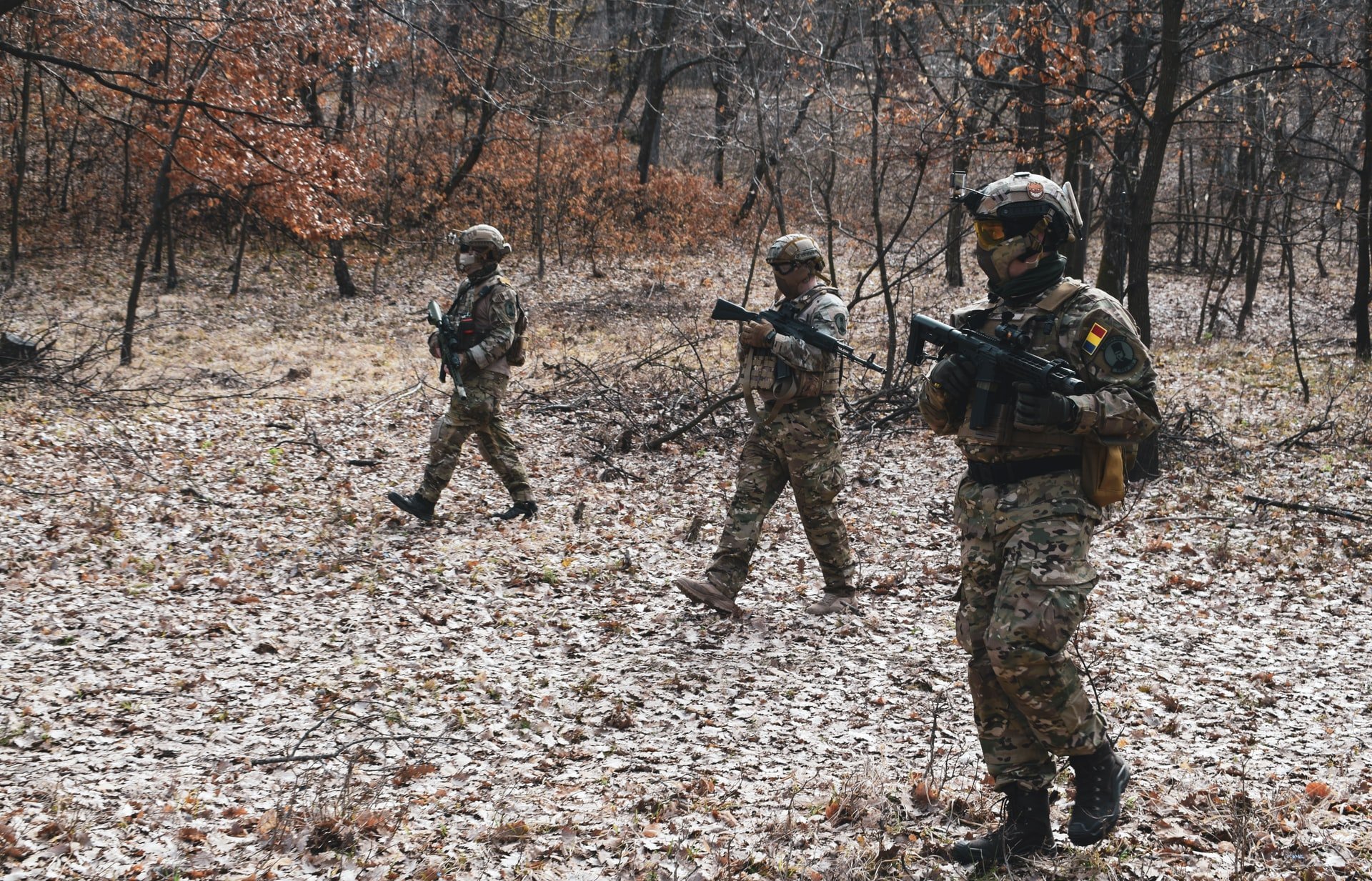 Três pessoas com roupas camufladas, armadas, andando em floresta