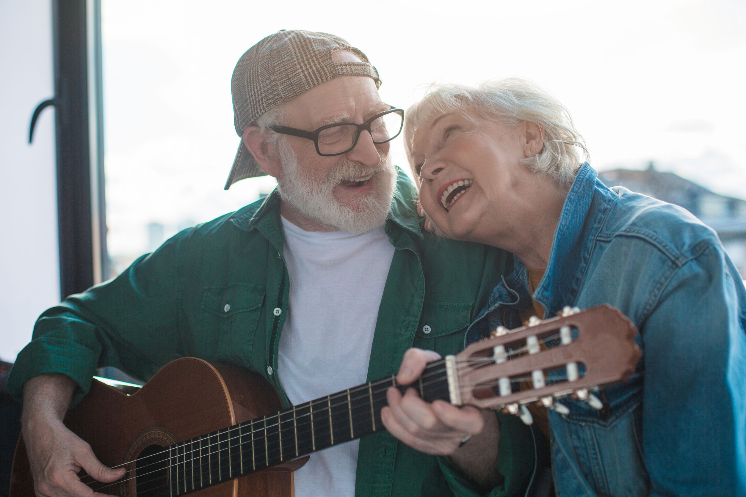 Homem idoso e tocando violão para senhora e os dois estão sorrindo