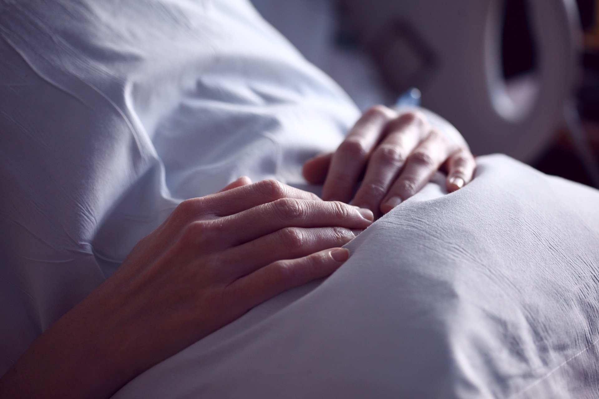 Pessoa deita em cama de hospital com as mãos sobre a barriga