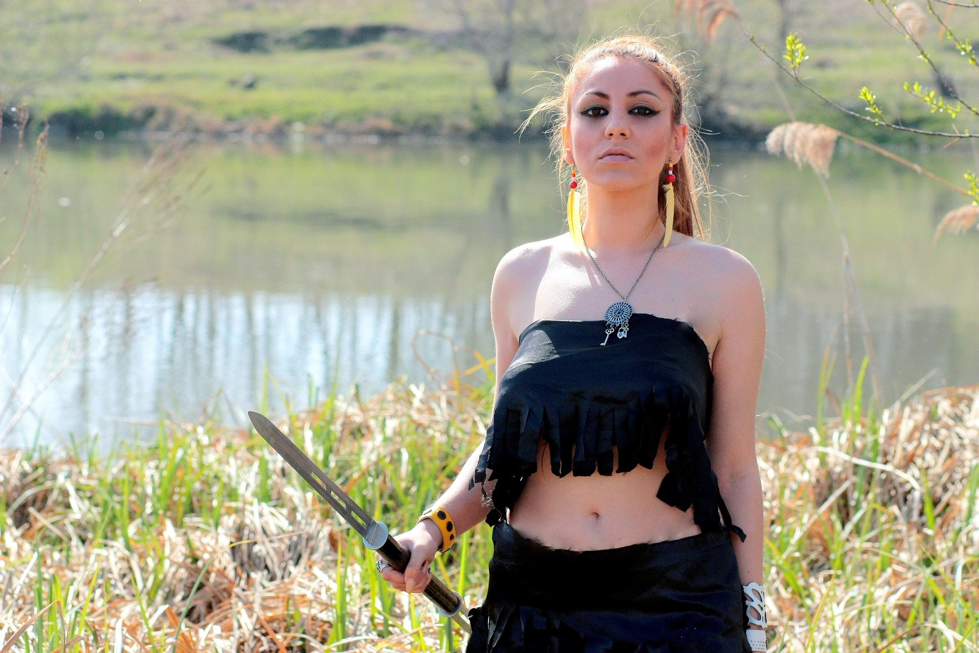 Mulher segurando espada perto de lago