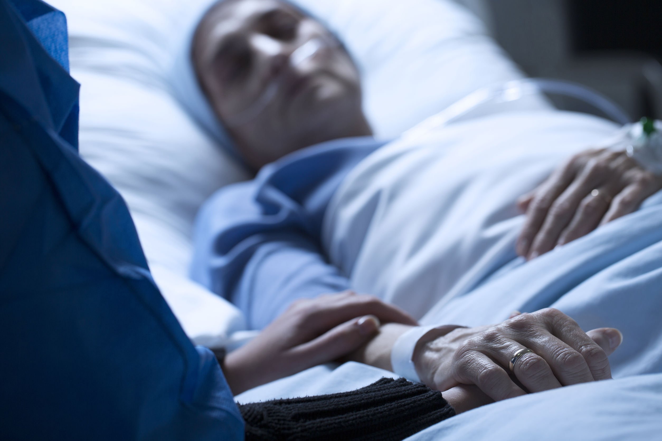 Paciente em cama de hospital e pessoa segurando sua mão