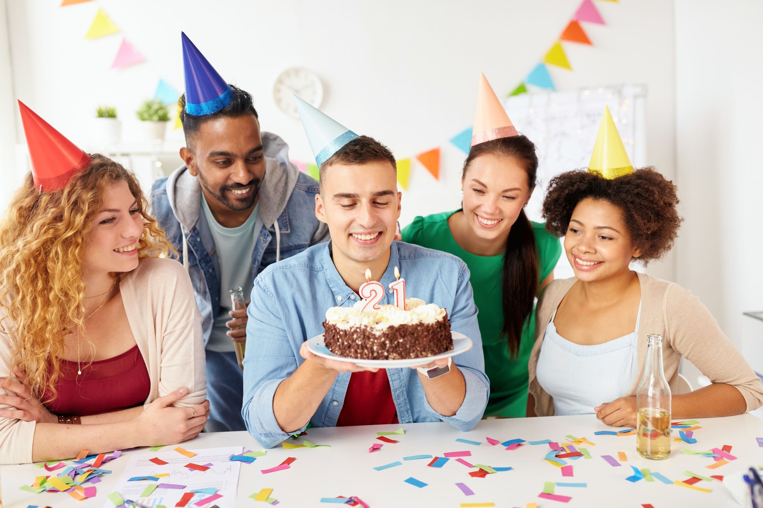 Homem sentado segurando bolo de aniversário cercado de amigos