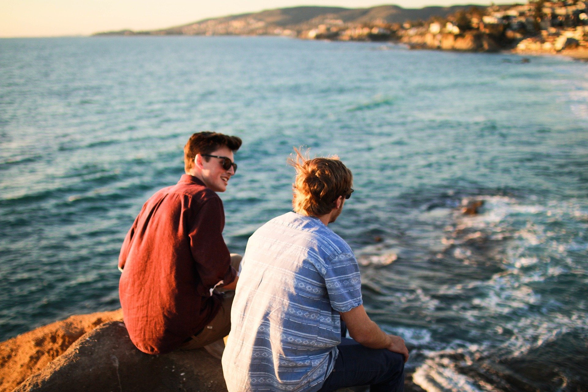 Amigos sentados em pedra perto do mar, rindo e conversando
