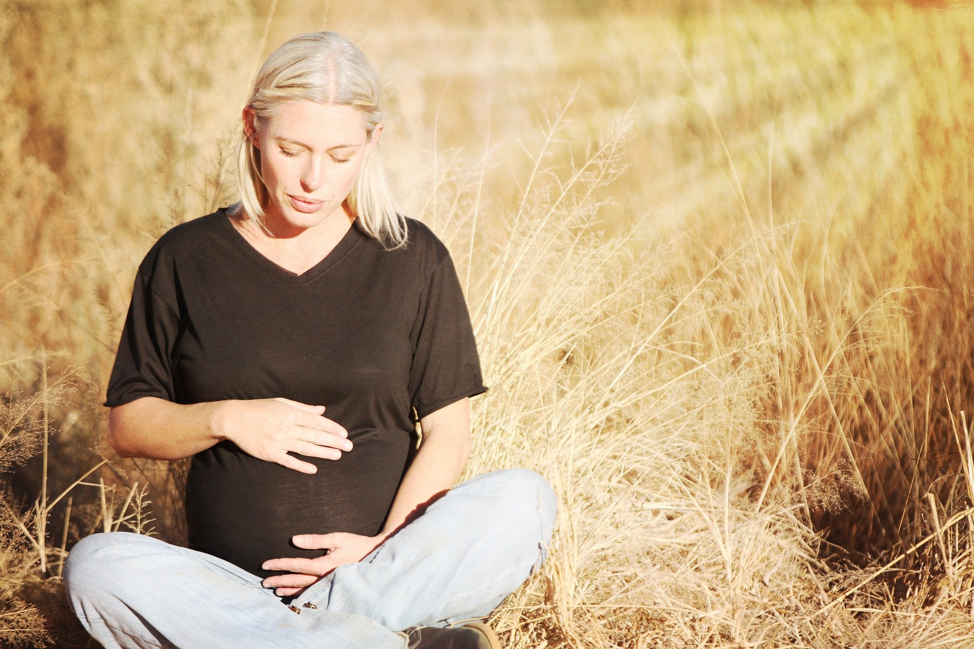 Mulher grávida com as mãos sobre a barriga sentada em campo