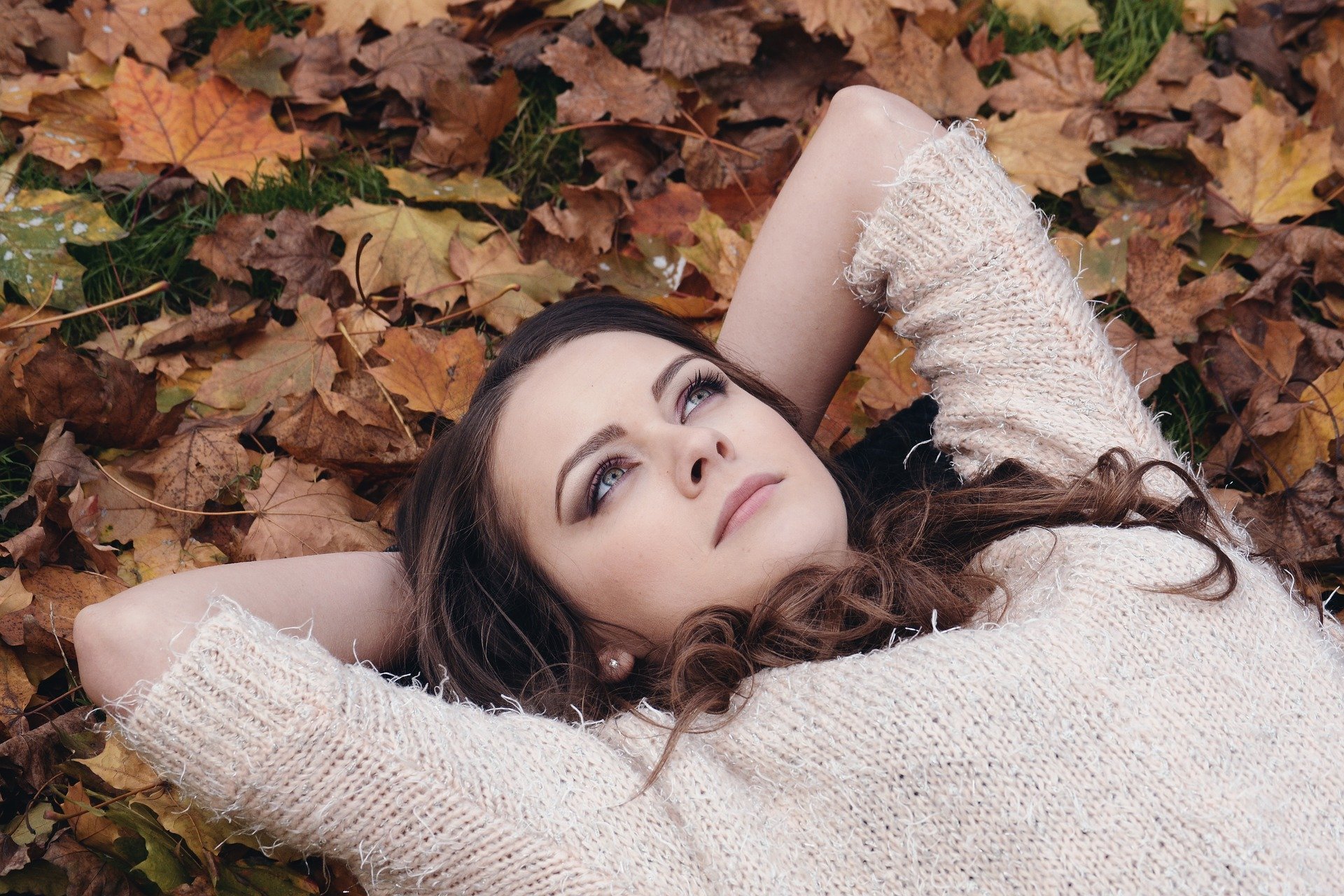 Mulher deitada sobre monte de folhas secas, com expressão pensativa