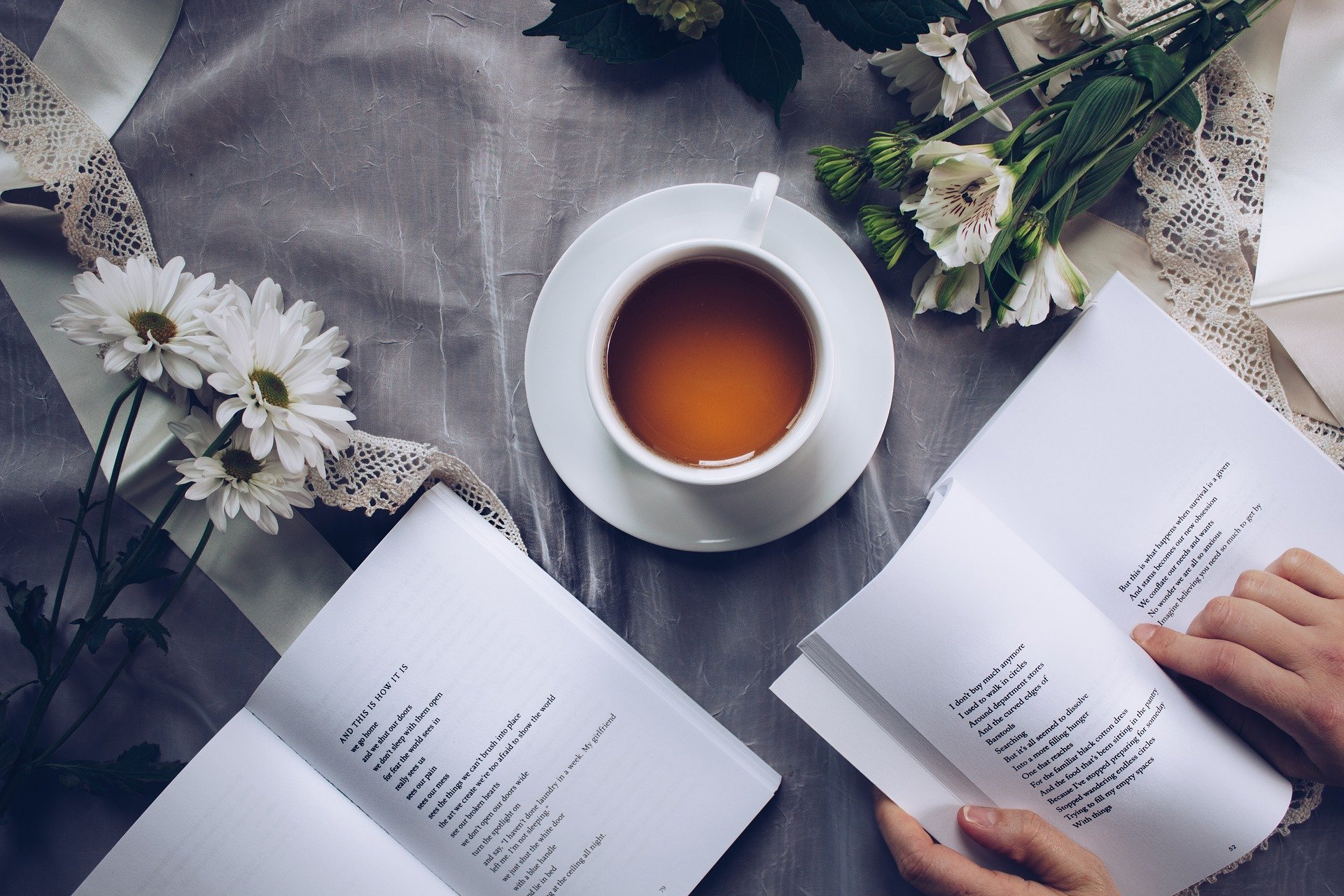 Pessoa lendo livro ao lado de flores e uma xícara de chá