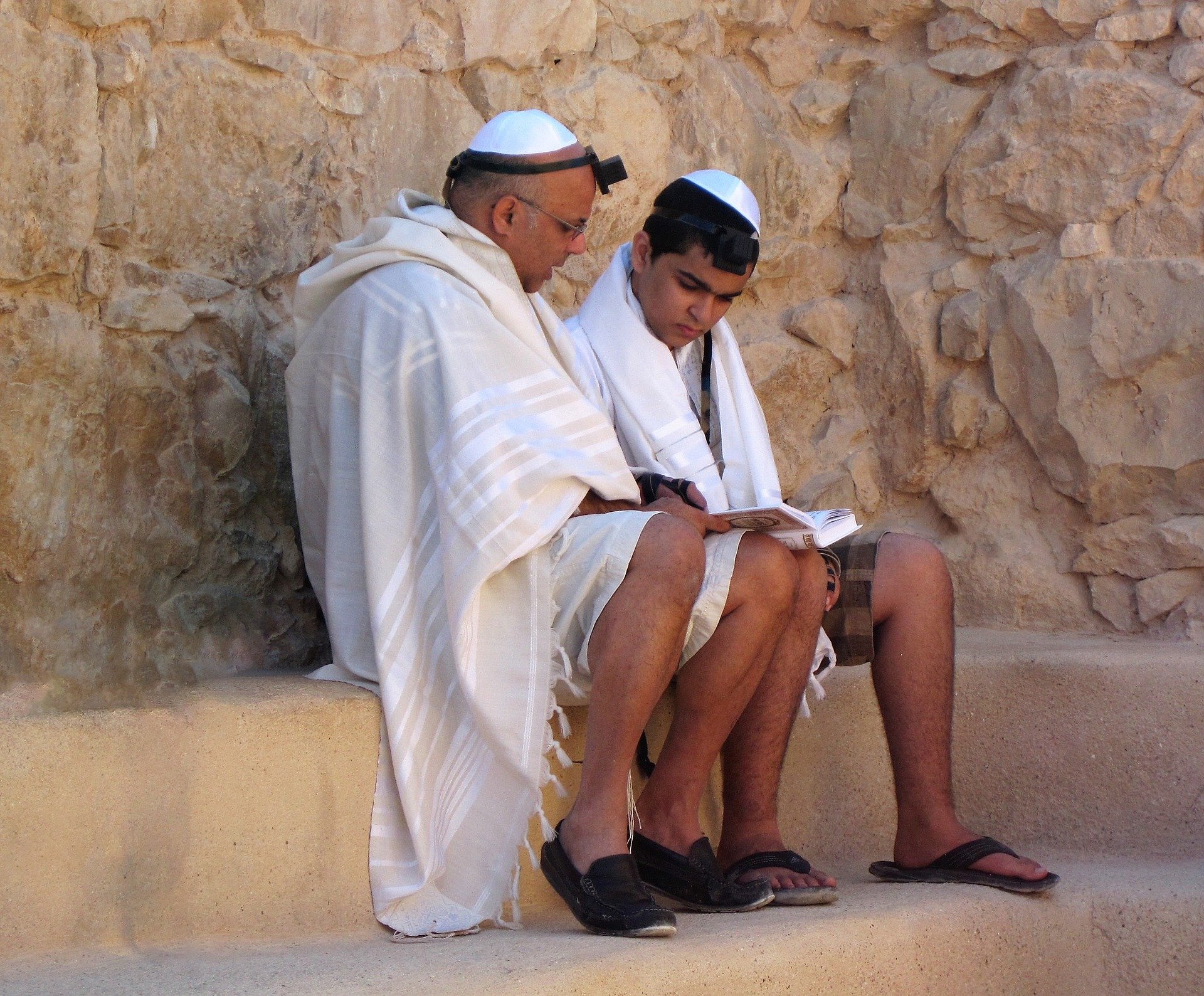 Pai e filho sentados lendo torá, ambos usando roupas tradicionais do judaísmo