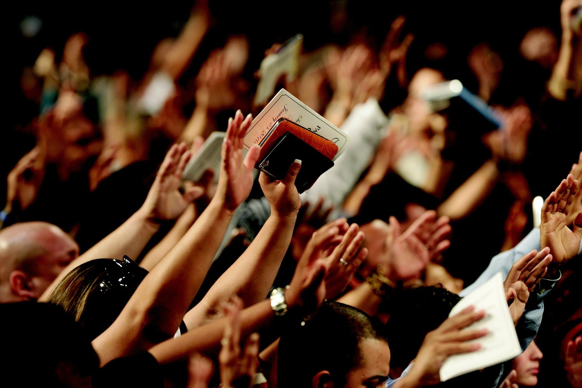 Pessoas com as mãos para o alto segurando bíblias durante culto