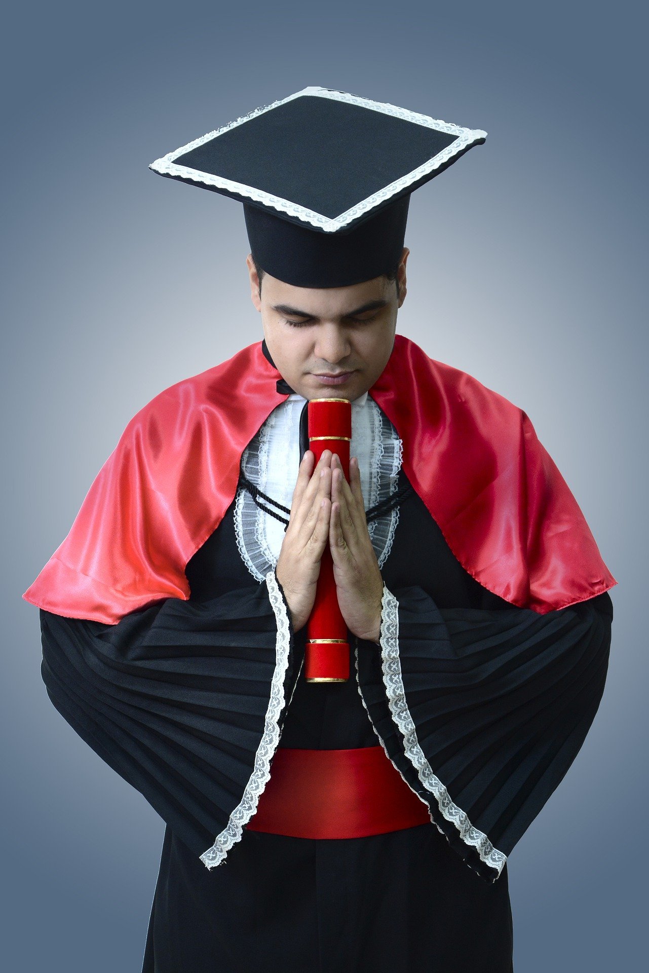 Homem formando de cabeça baixa segurando diploma, vestindo capelo e beca