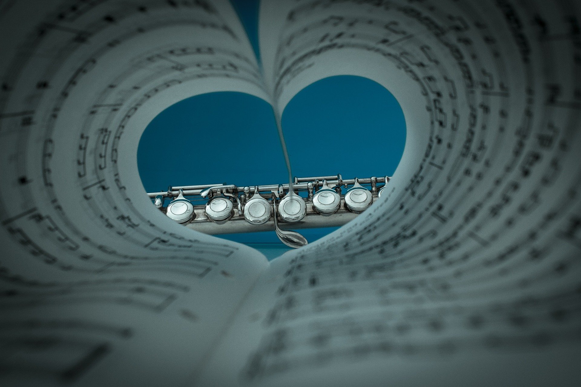 Folha de partitura musical dobrada em forma de coração,  instrumento musical aparecendo ao fundo