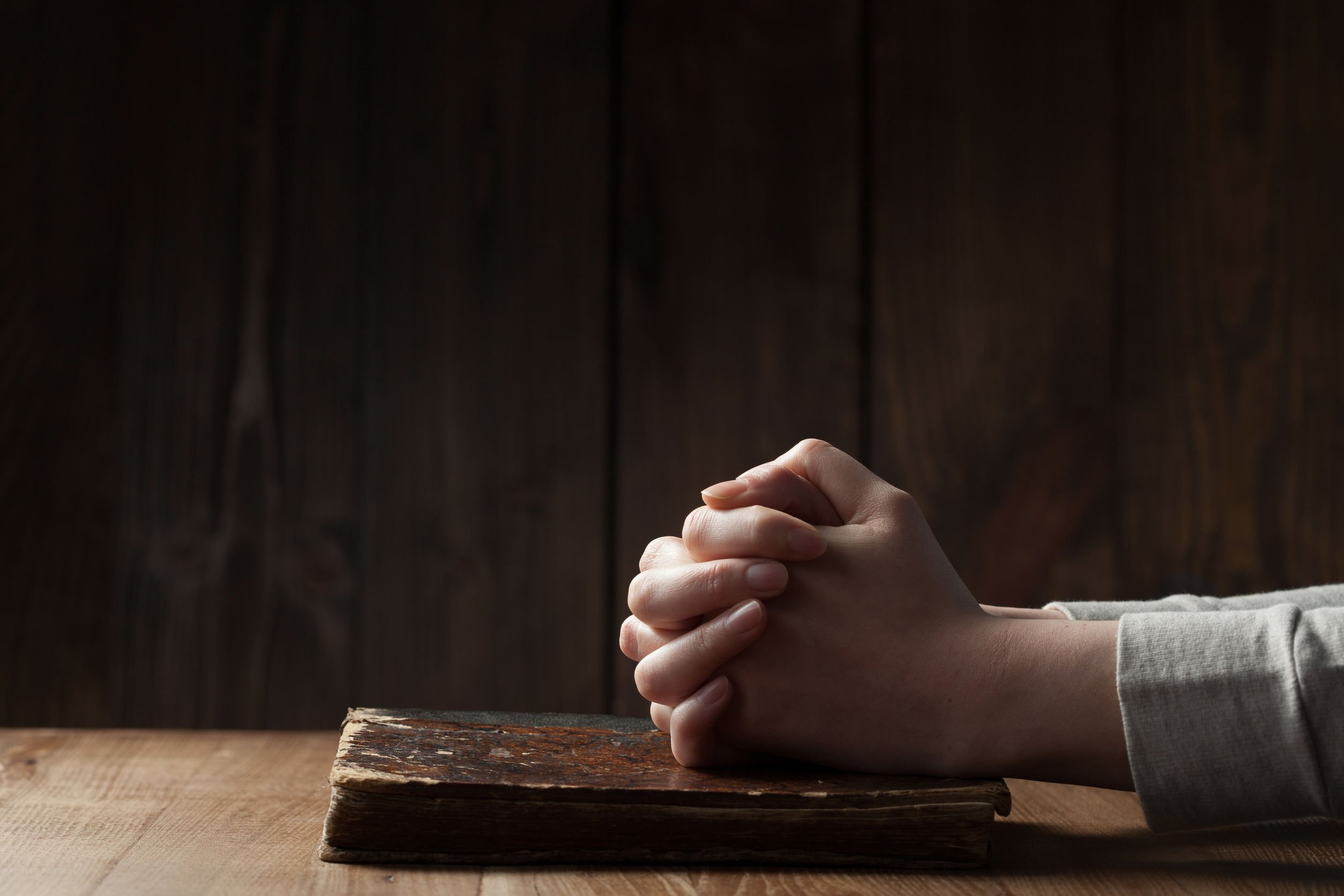 Mão de pessoa orando sobre bíblia