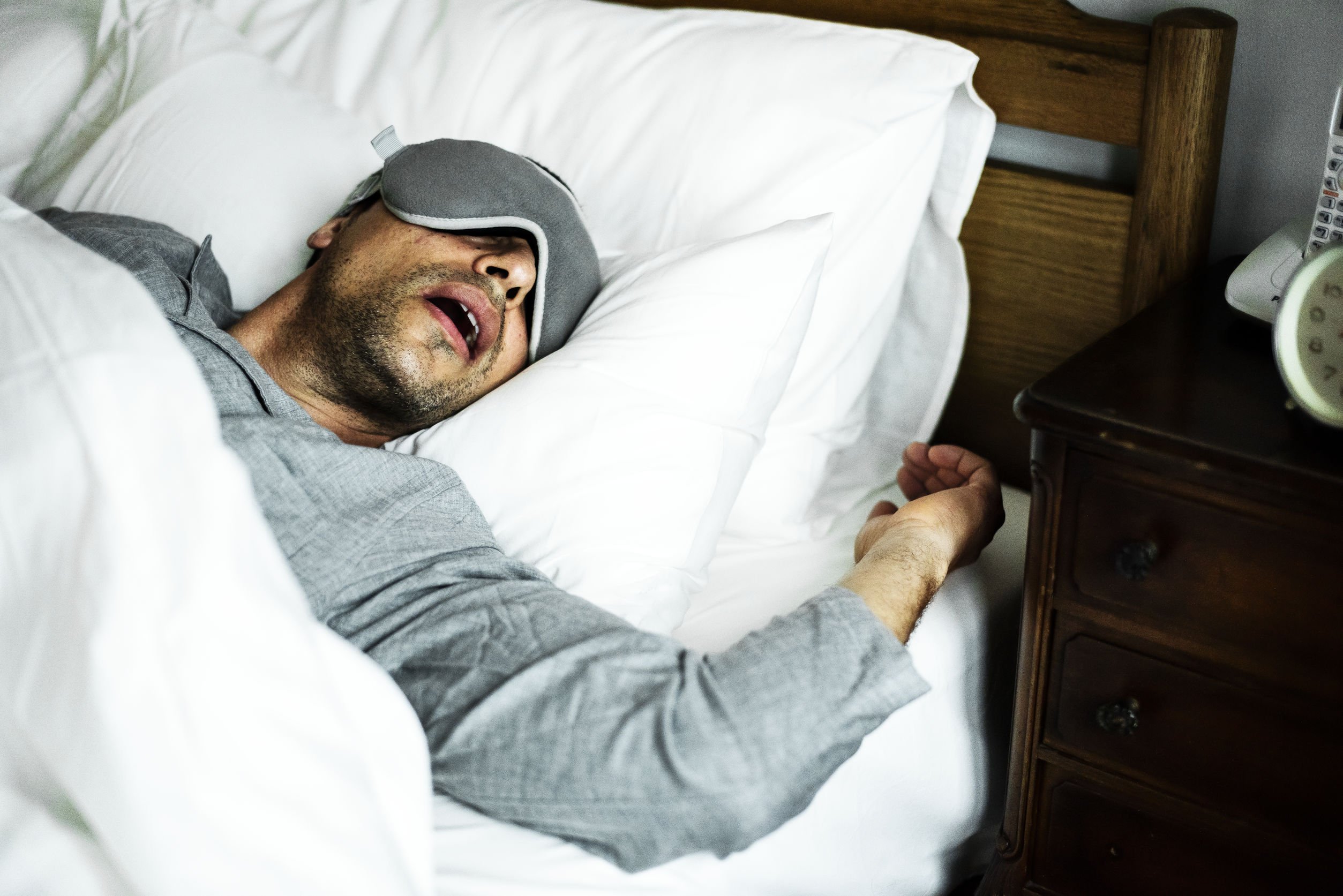 Homem dormindo de boca aberta em cama branca