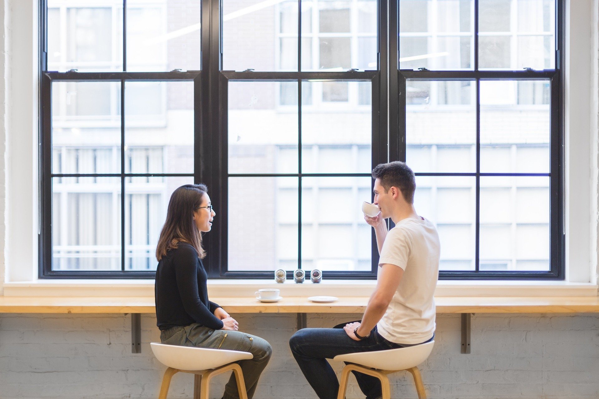 Homem e mulher conversando sentados em mesa de café em frente à várias janelas