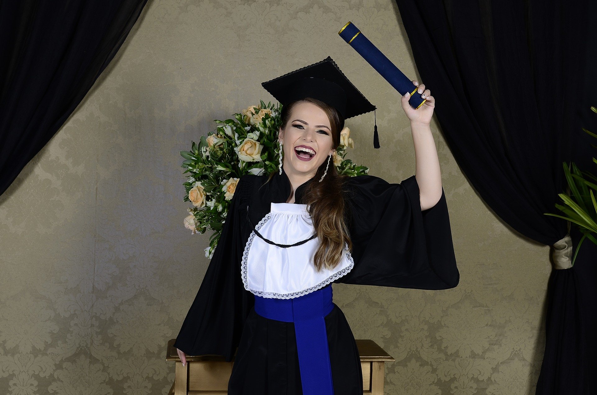 Mulher sorrindo segurando diploma usando beca e capelo