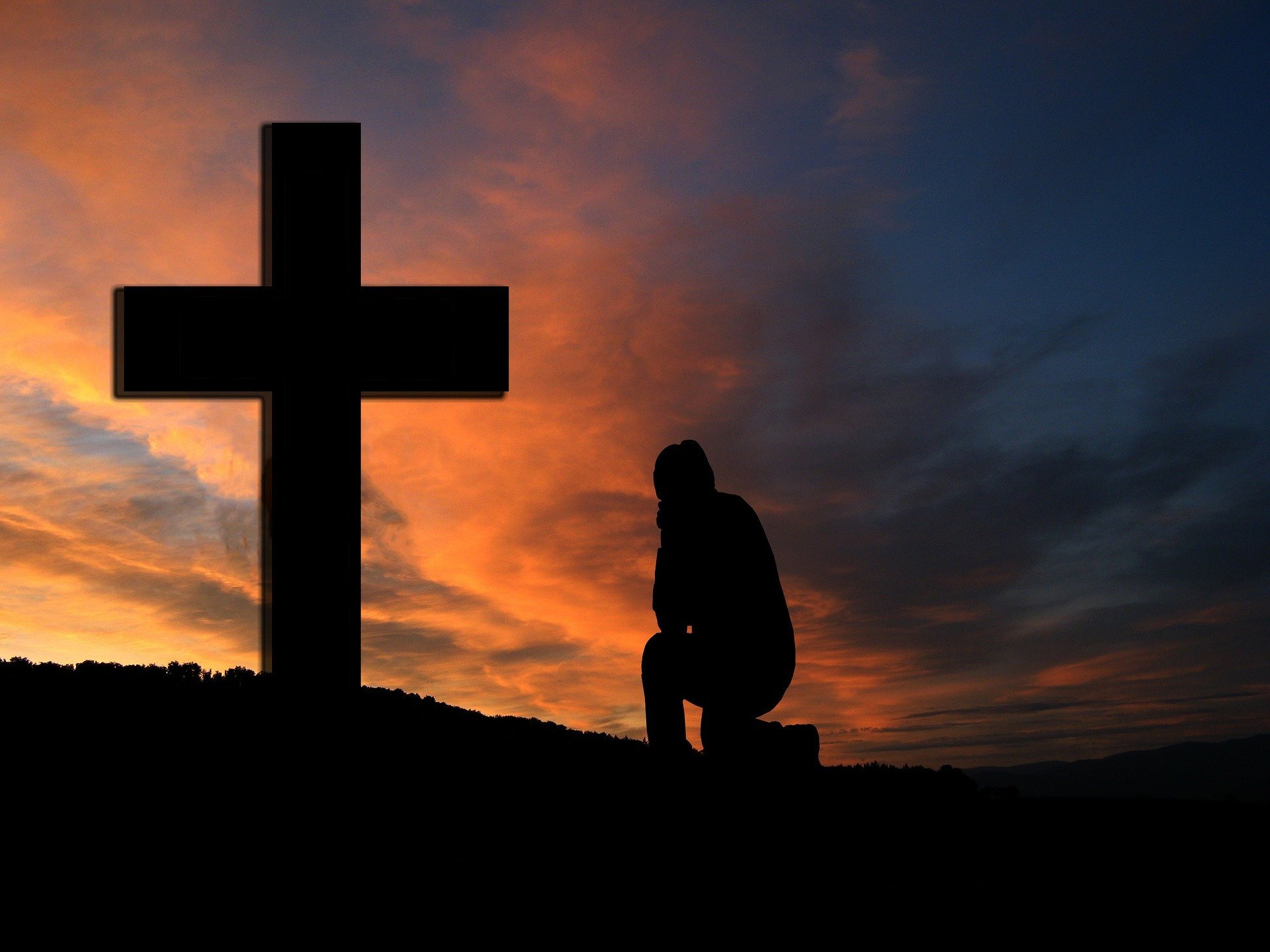 Silhueta de cruz e de homem ajoelhado orando
