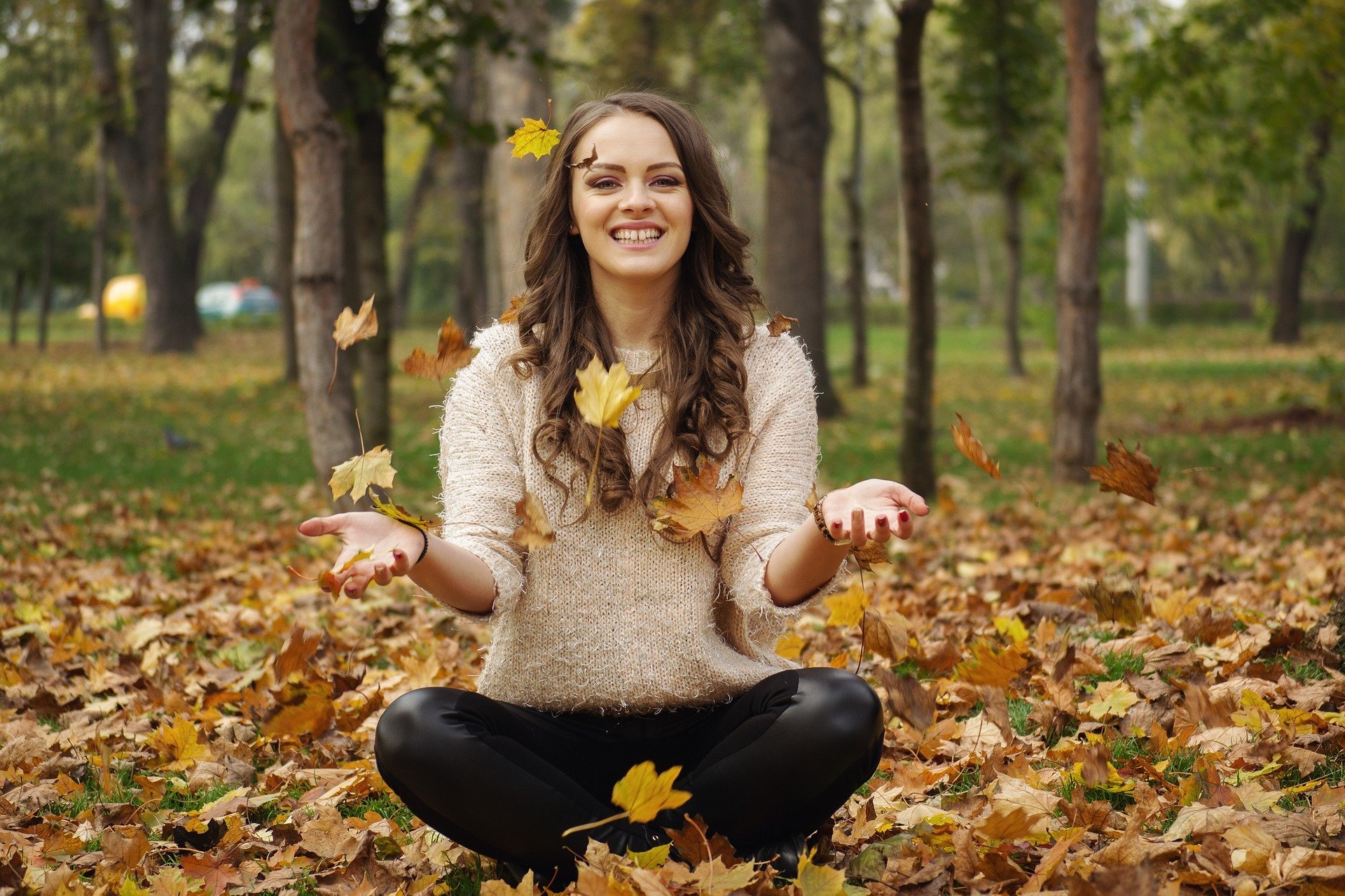 Mulher sorrindo sentada em pilha de folhas secas em parque