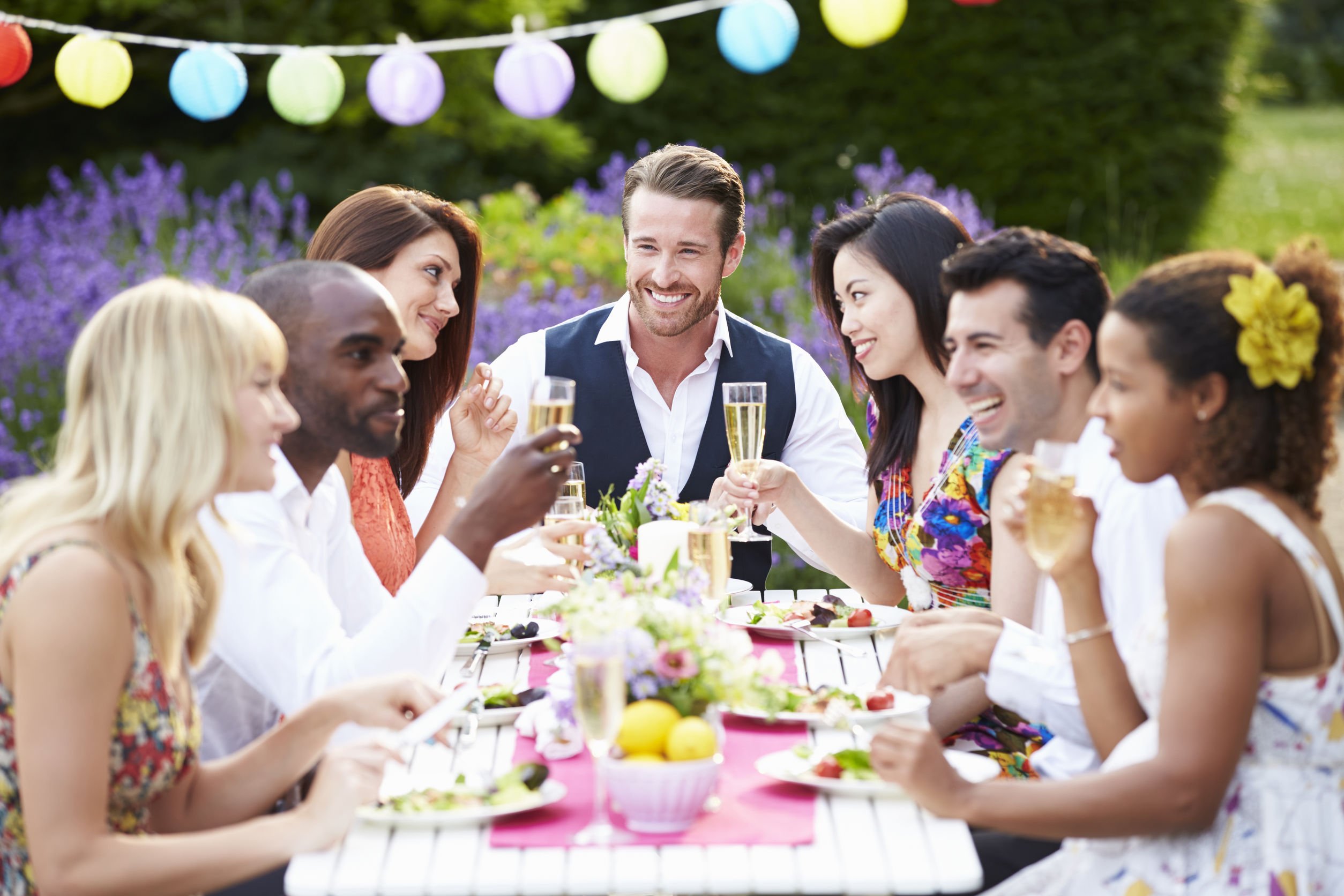 Pessoas comemorando enquanto comem e bebem ao ar livre, todos sentados em mesa