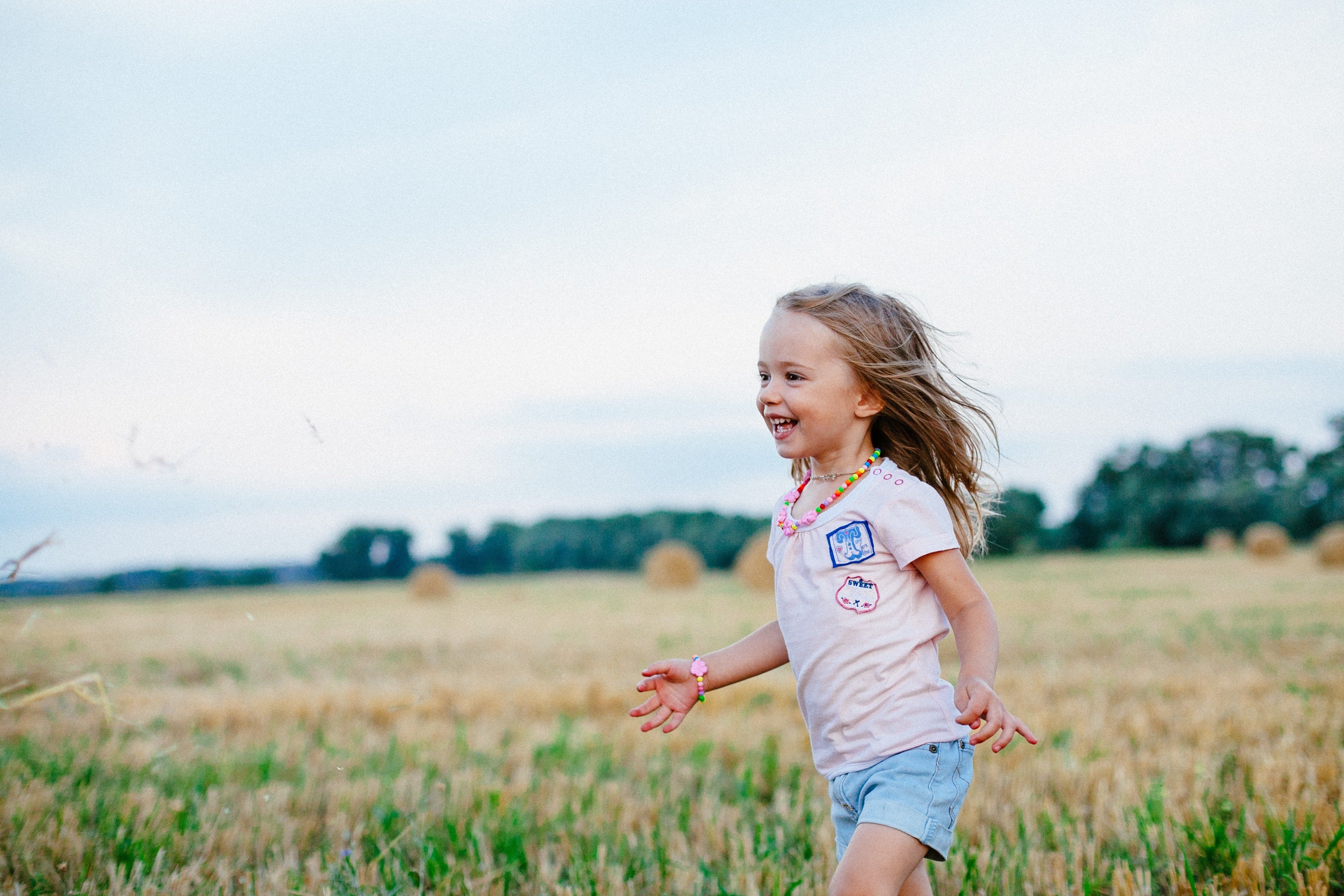 Criança branca de cabelos loiros correndo ao ar livre, em meio a grama baixa, com expressão feliz