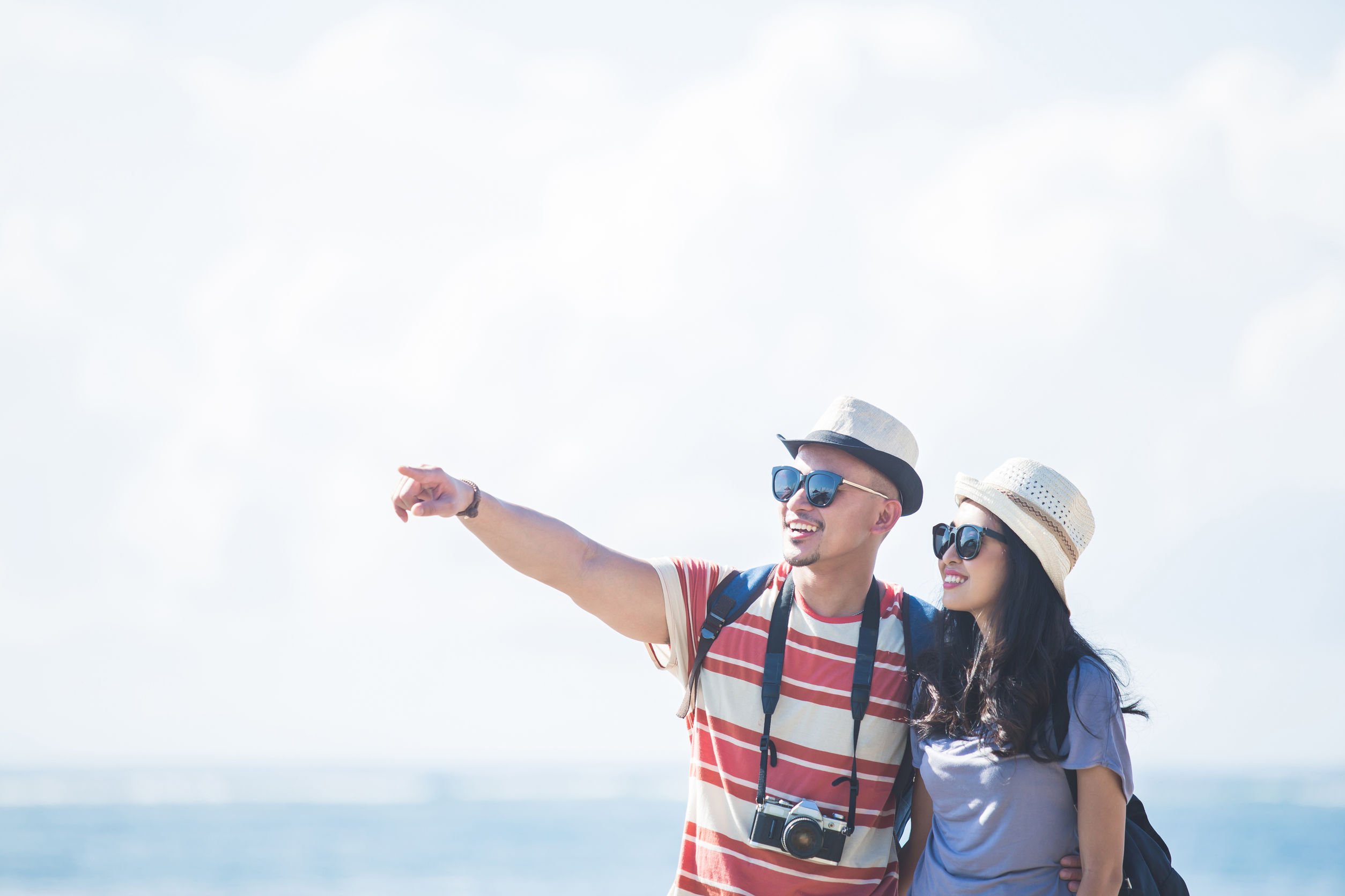 Homem e mulher ao ar livre, ambos usando óculos escuros e chapéu, caracterizados como turistas