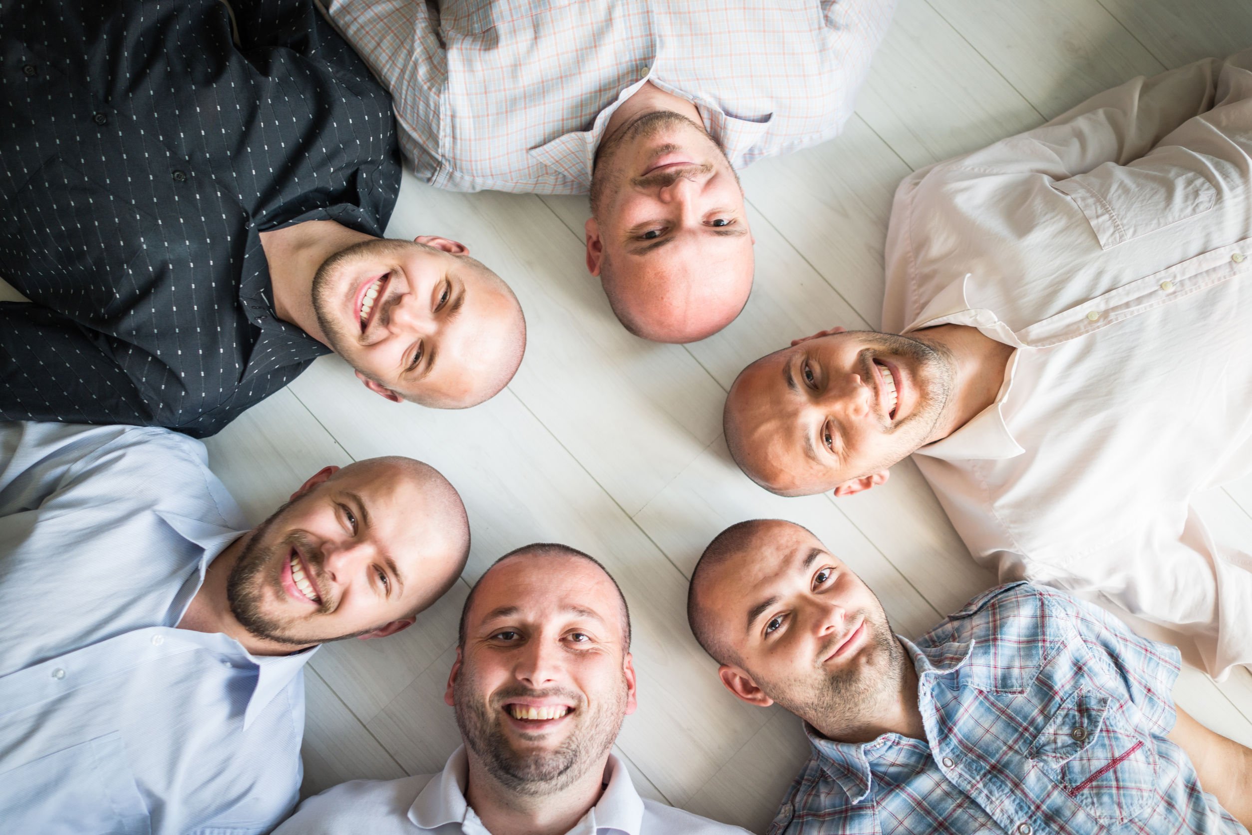 Grupo de homens com o cabelo raspado, deitados no chão, formando um círculo