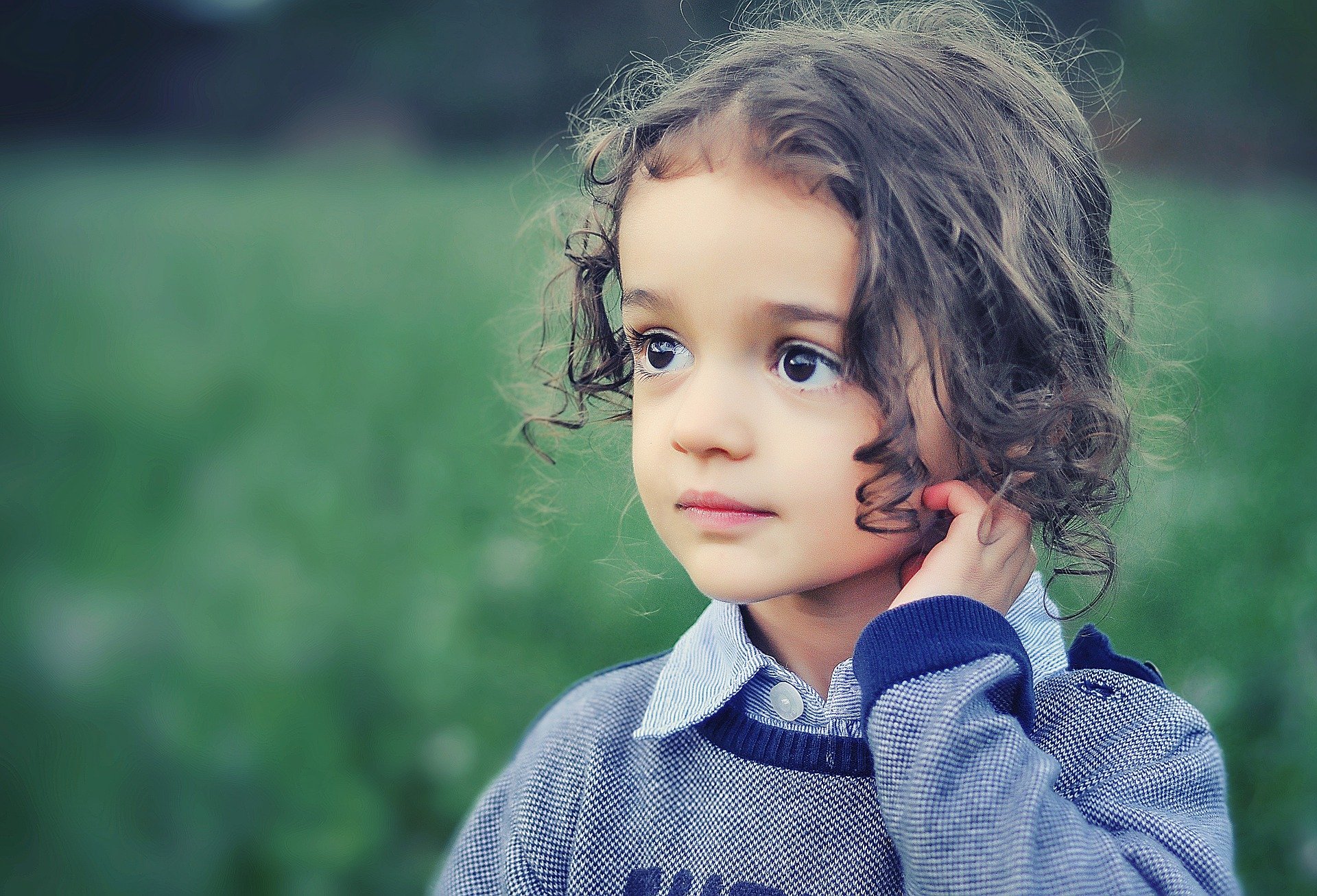 Menina pequena, com a mão no cabelo, em campo de vegetação