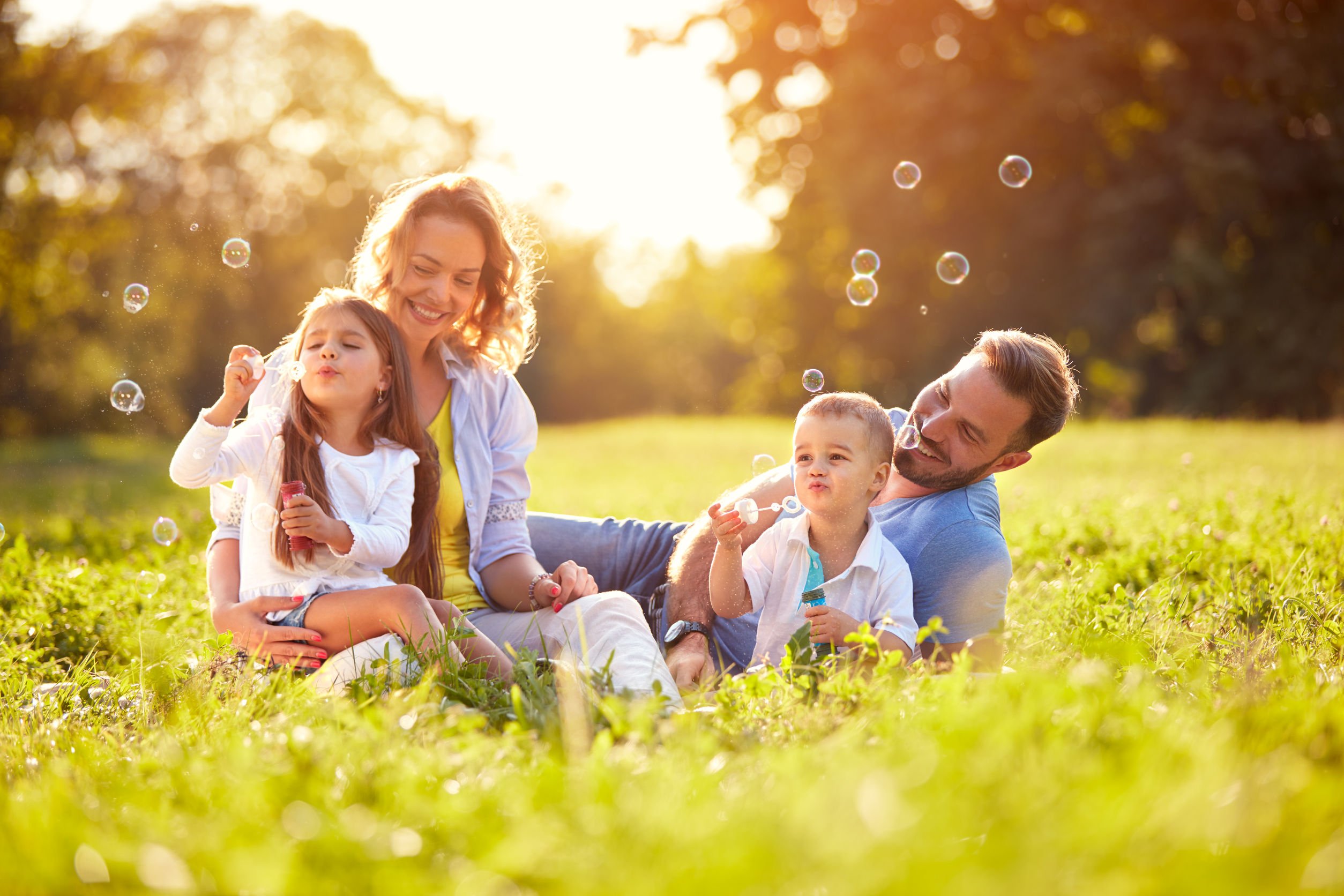 Família sentada em campo, sorrindo e brincando com bolhas de sabão