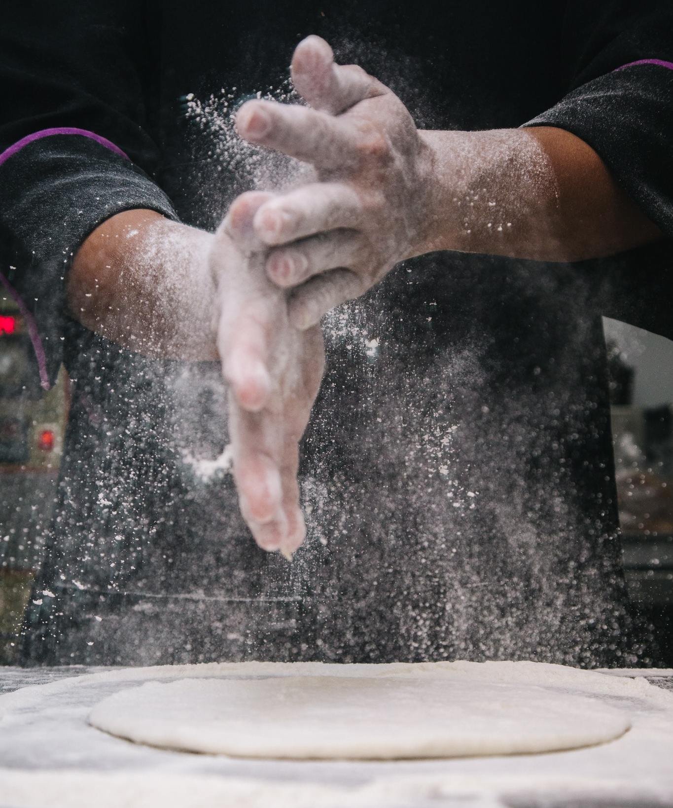 Mãos cobertas de farinha sob um massa aberta na bancada.