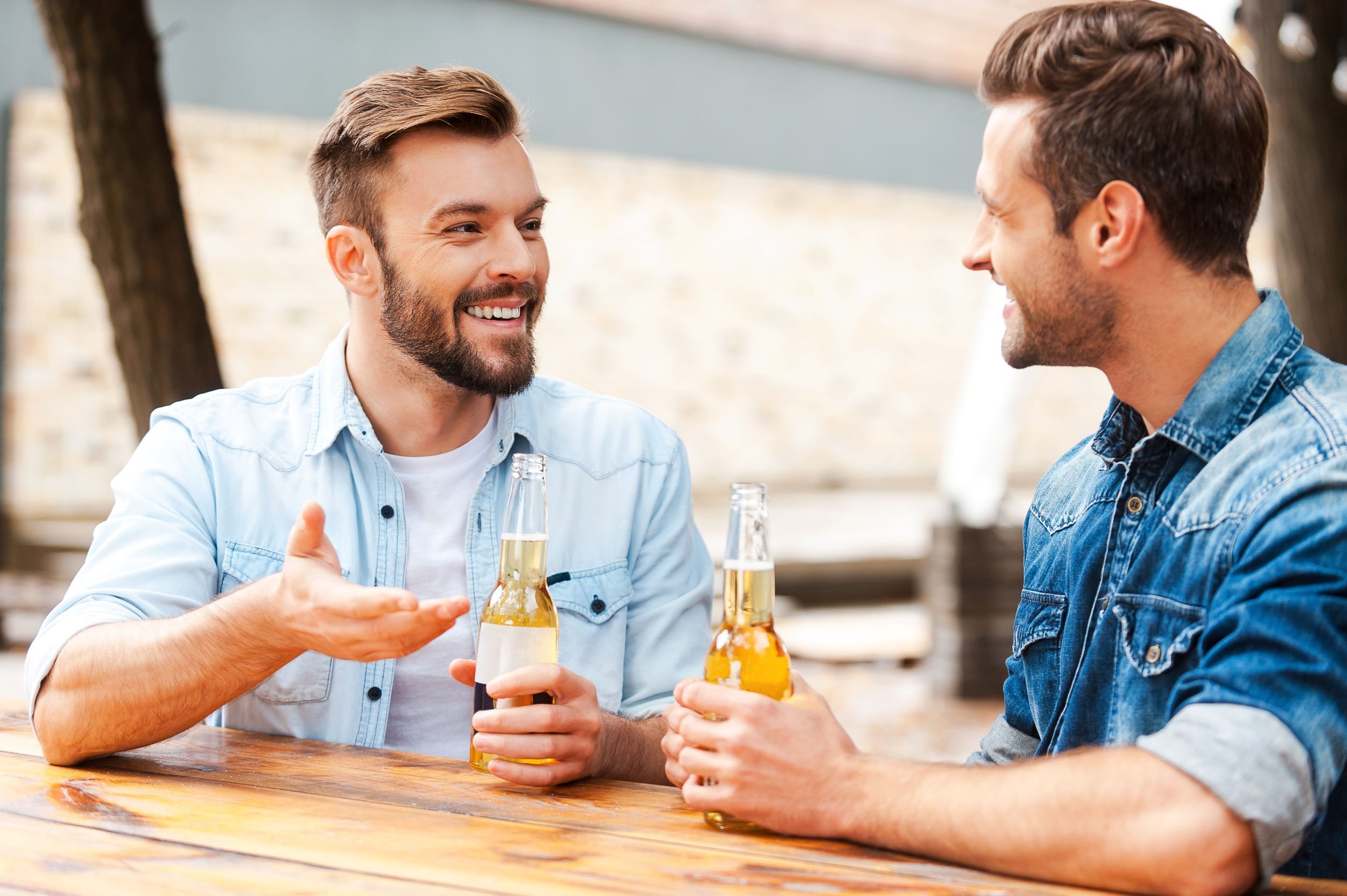 Homens bebendo cerveja e conversando em mesa de bar ao ar livre