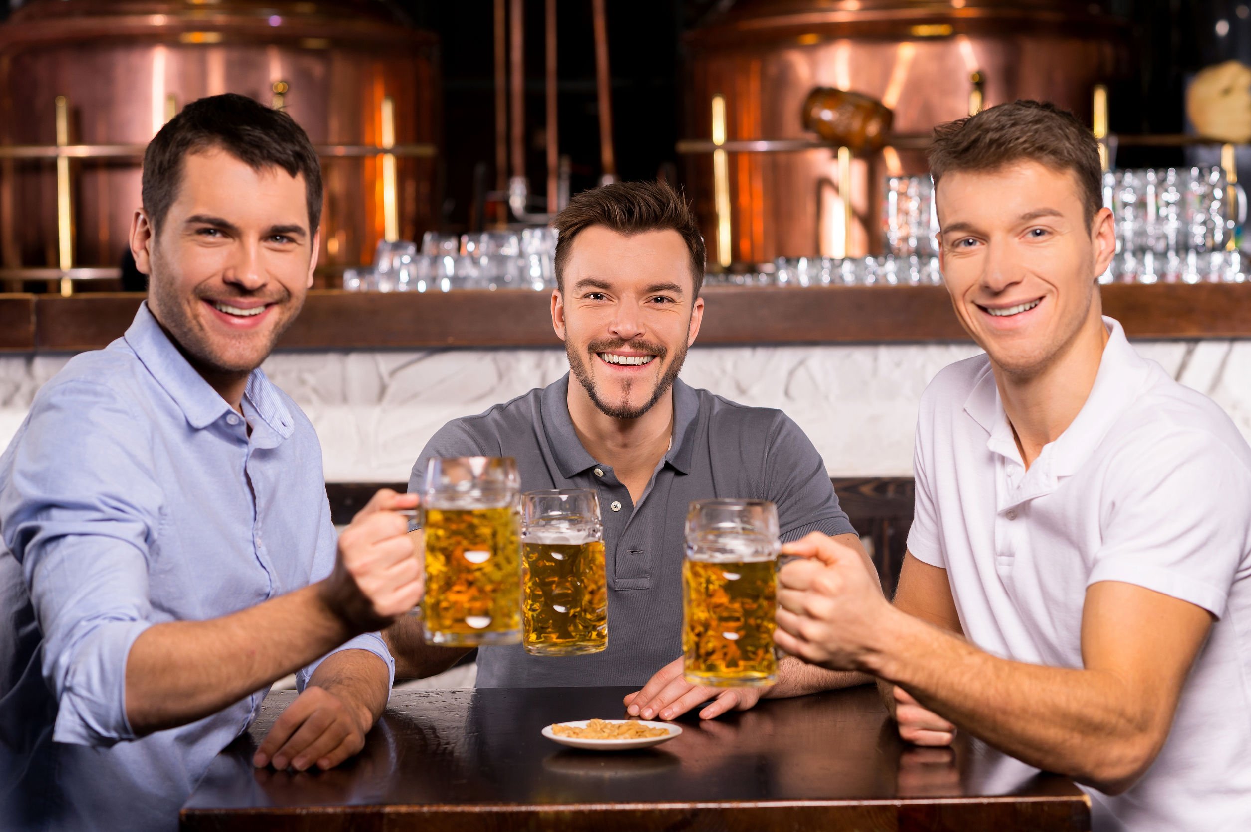 Homens brindando e sorrindo em mesa de bar