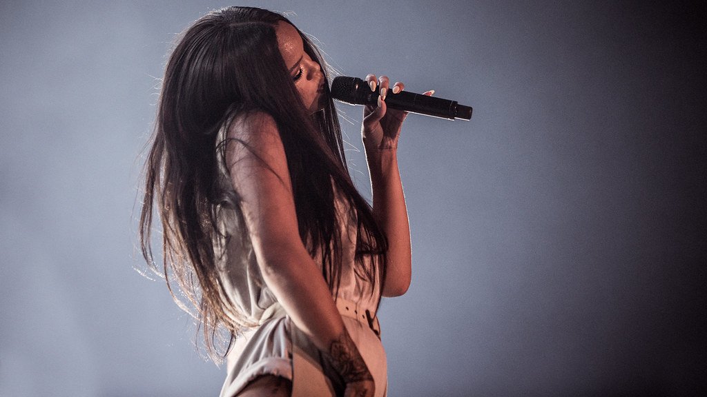 Cantora Rihanna com cabelos longos e pretos com cabeça inclinada e microfone à boca.