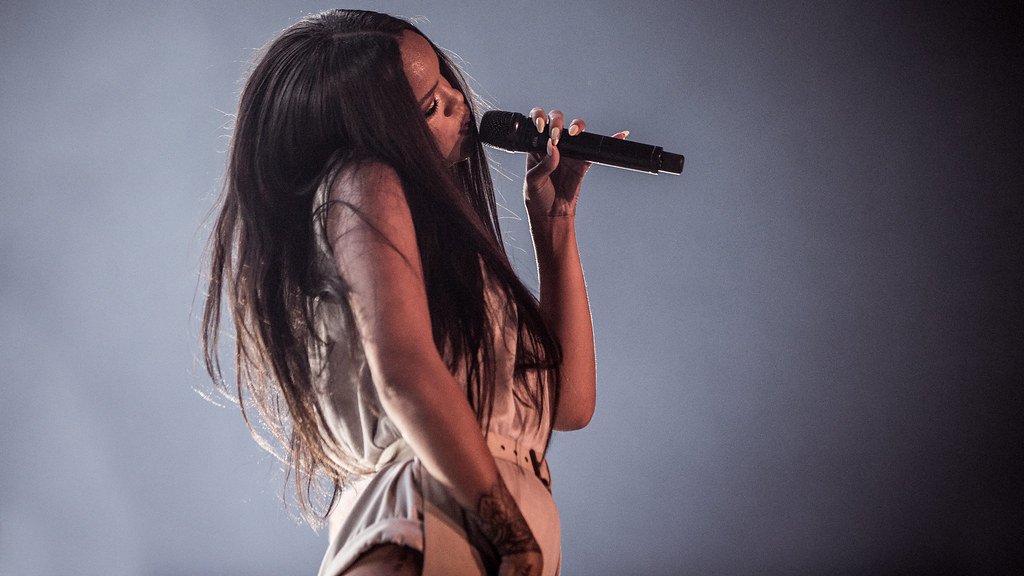 NRK P3 / VisualHunt Cantora Rihanna com cabelos longos e pretos com cabeça inclinada e microfone à boca.