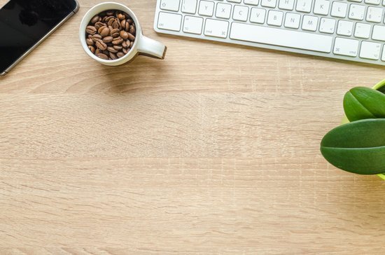 Lukas/Canva Mesa de escritório com uma caneca de grãos de café uma planta ao lado