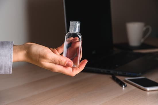 Pessoa segurando um fraco de álcool em gel ao lado de uma mesa de escritório