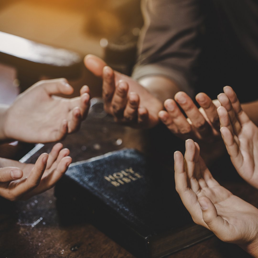 Imagem de pessoas orando juntas em uma mesa. Uma bíblia se encontra no meio da mesa.