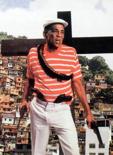 Músico Bezerra da Silva segurando duas pistolas. Ao fundo, uma favela.