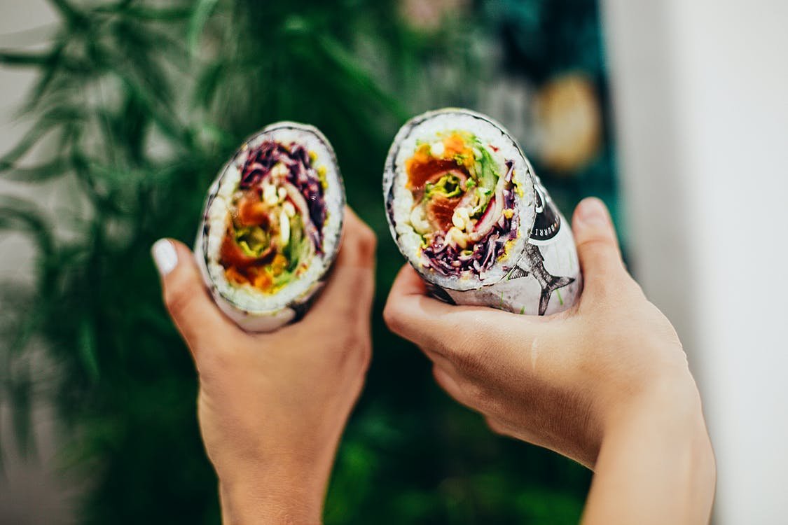 Mãos de duas pessoas segurando burritos veganos