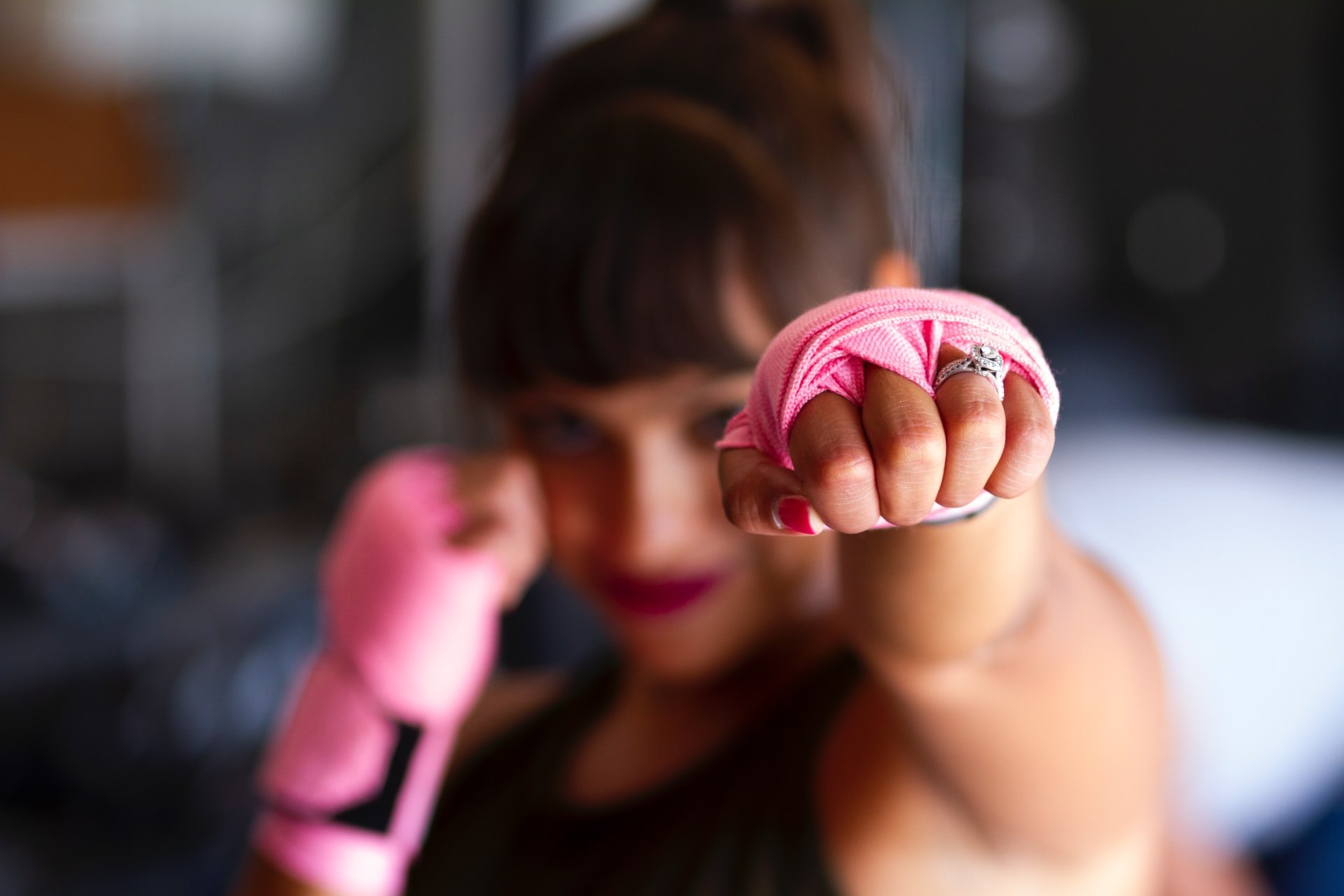 Mulher, lutadora, com as mãos enroladas em faixas cor de rosa para colocar luva de box.