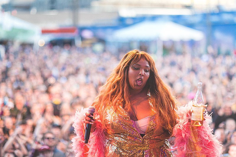 Cantora Lizzo em apresentação de show com garrafa de água na mão e microfone na outra