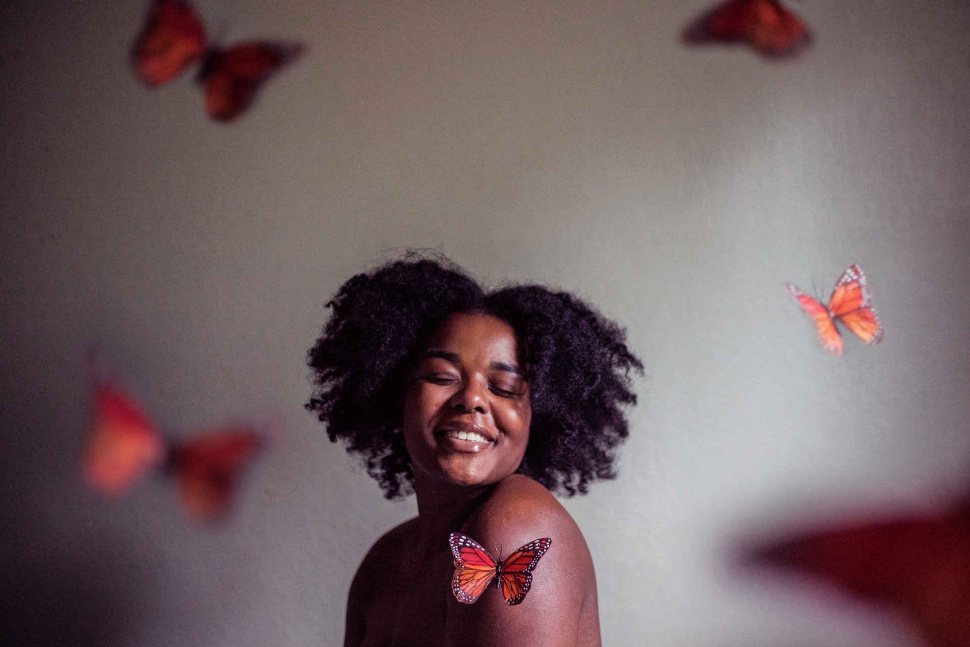 Jessica Felicio / Unsplash Mulher negra rodeada por borboletas laranjas.