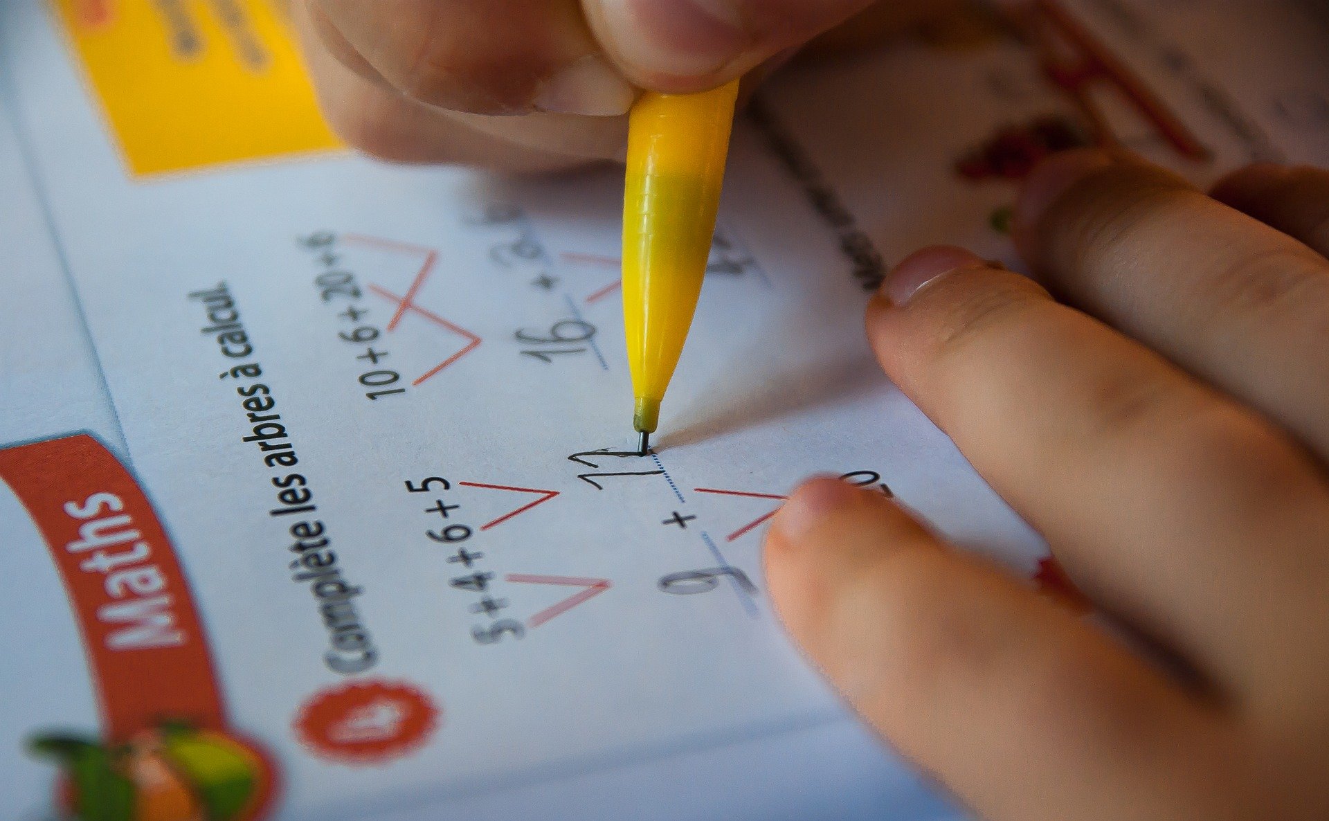 Mão de criança fazendo lição de matemática.